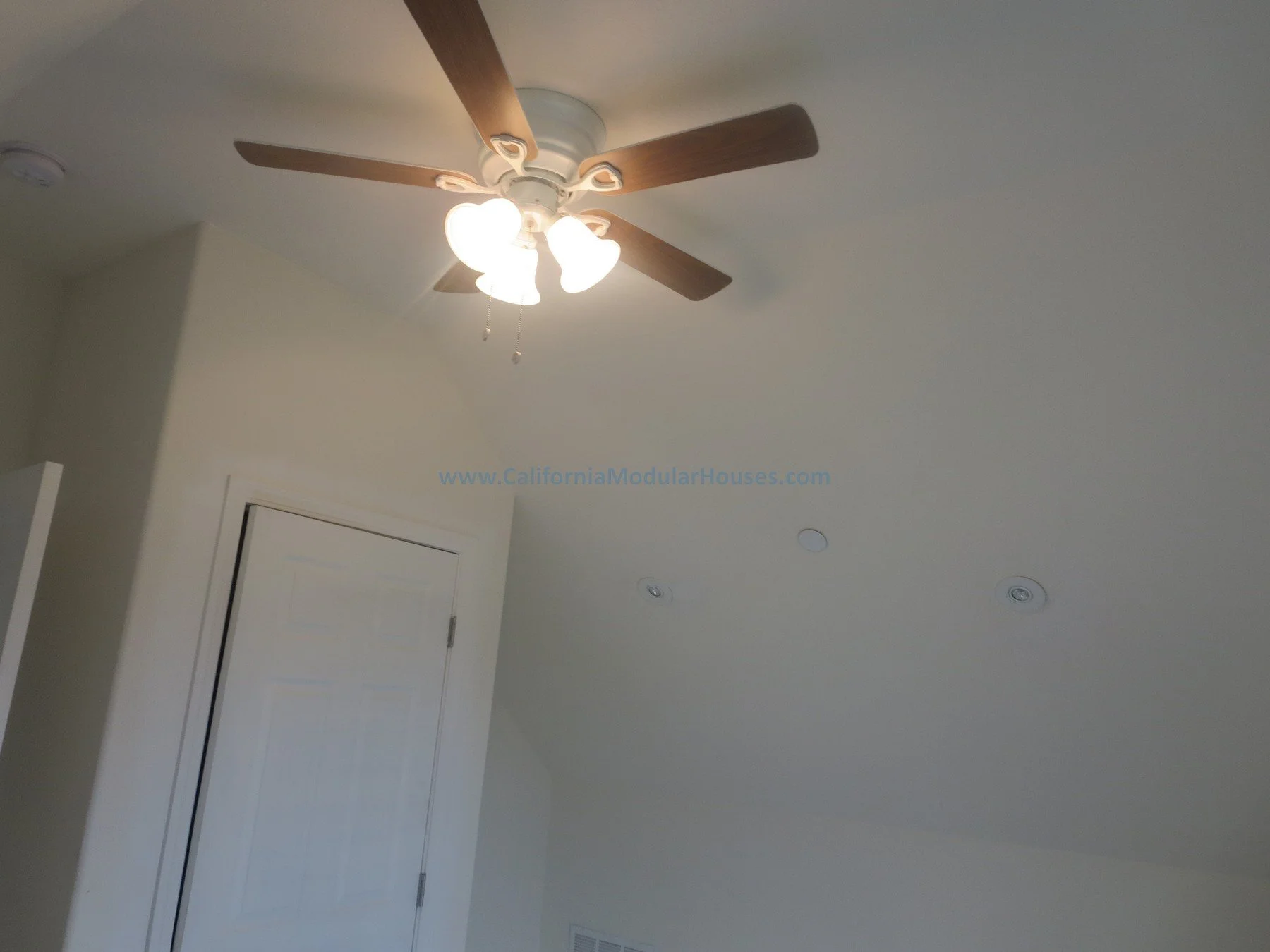 Interior ceiling with ceiling fan with light fixtures, two ceiling vents, and a closed door.  Unfinished attic.  New pre-fab modular house in Napa, California.  California modular home.  