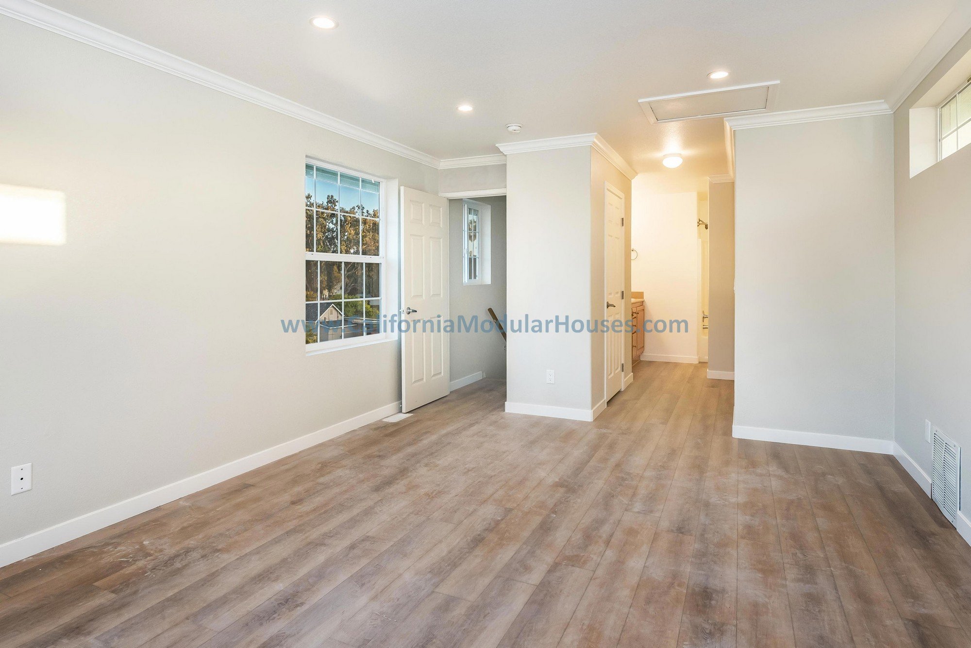 Great room with white walls, light wood flooring, a window, and a door leading outside.  Recess lighting.  Pre-fab modular homes for California.