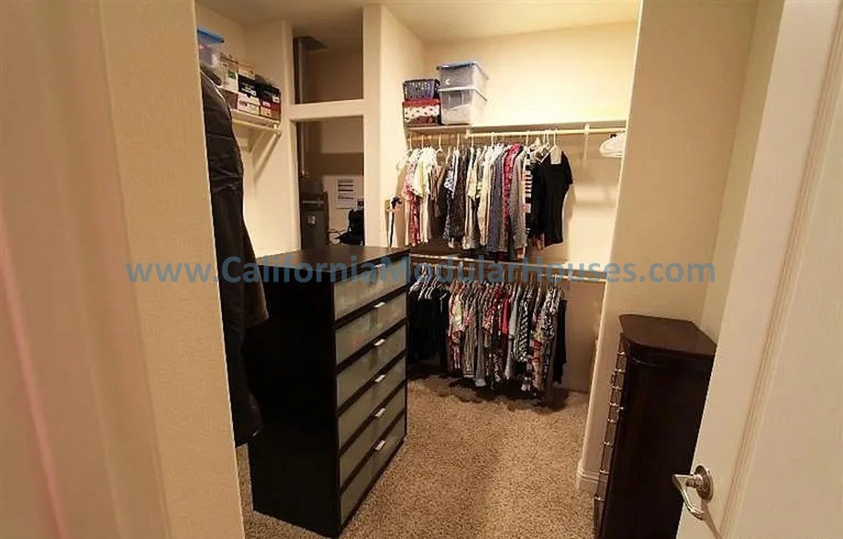 Small walk-in closet with clothing racks, shelves, and drawers filled with clothes and storage boxes.