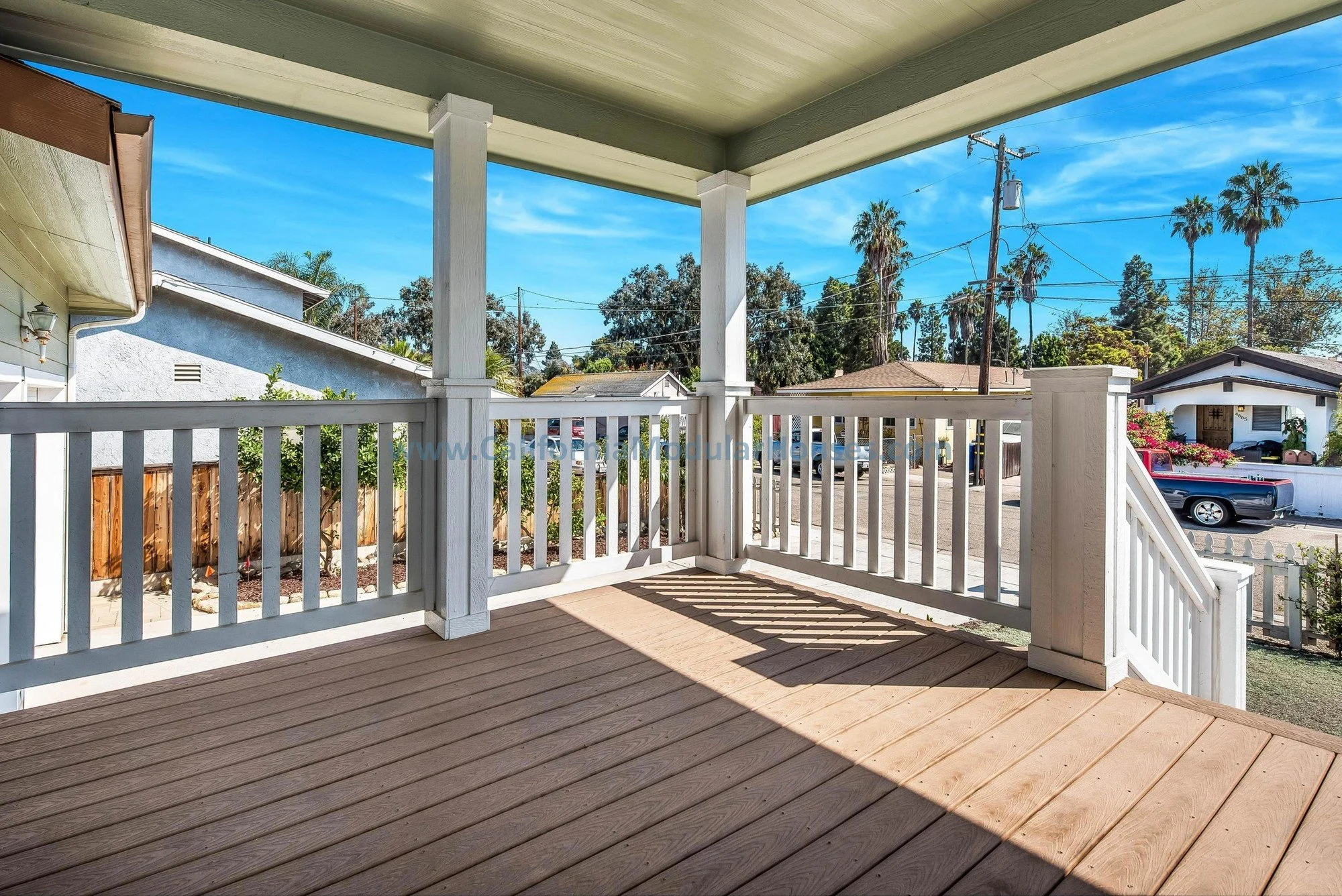 Sage green, brown trim prefab modular, two-story home. White door, white railing, brown covered porch.