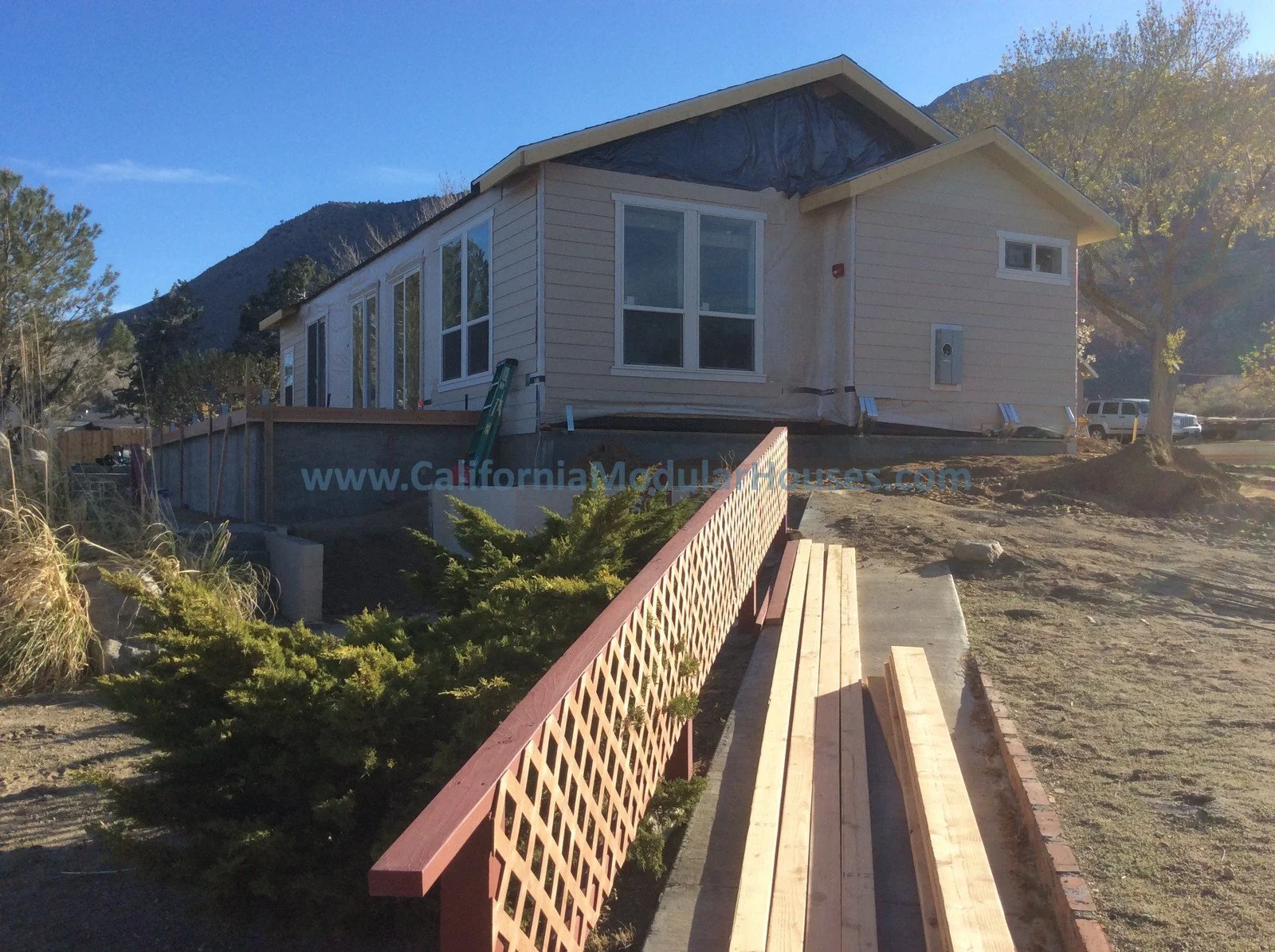 Under construction house with a beige exterior, large front windows, a wooden deck, and a mountain in the background.