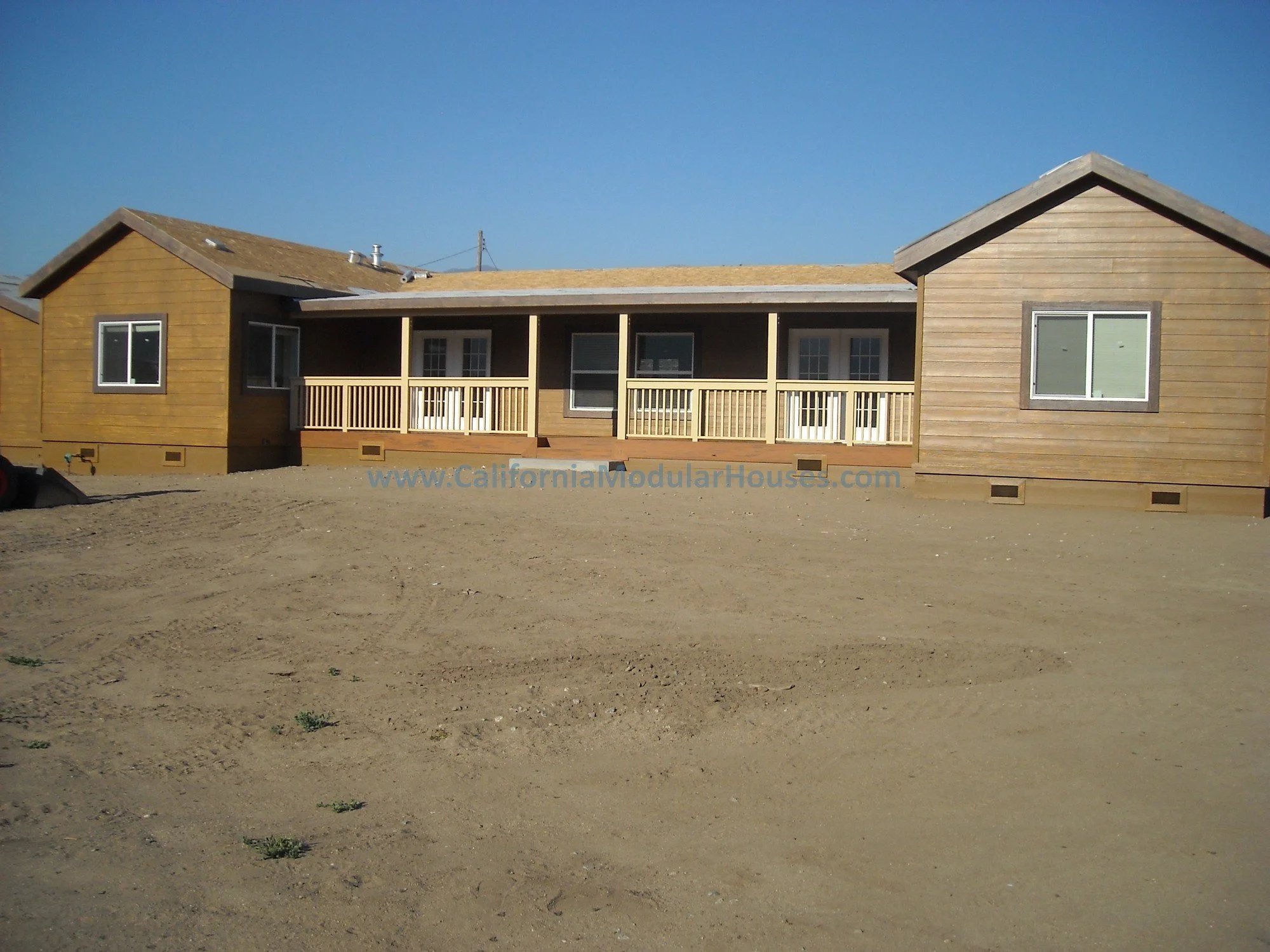 Newly constructed single-story modular home with a large rear porch, under a clear blue sky on a cattle ranch in Kern County.  