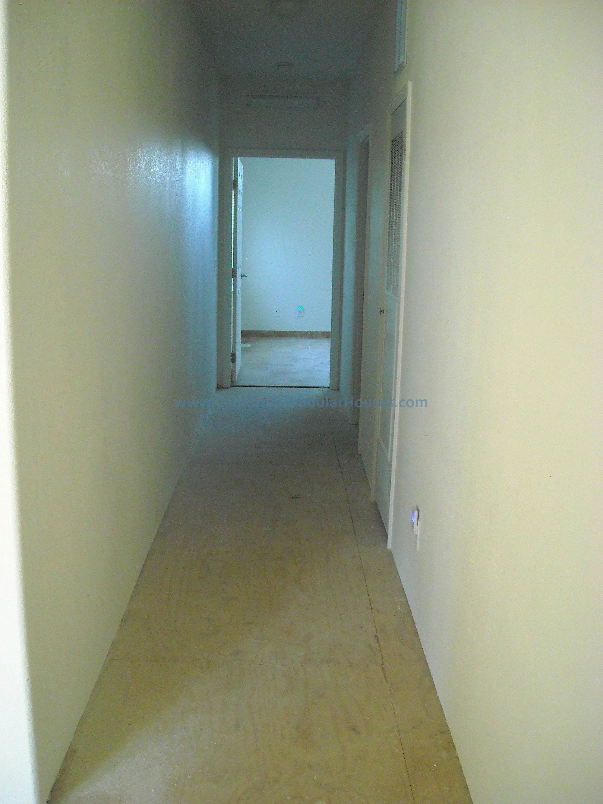 Empty hallway with yellow painted walls and beige floor, leading to a room with a door open to another room.  Factory-Built-Housing for California.  HCD.  