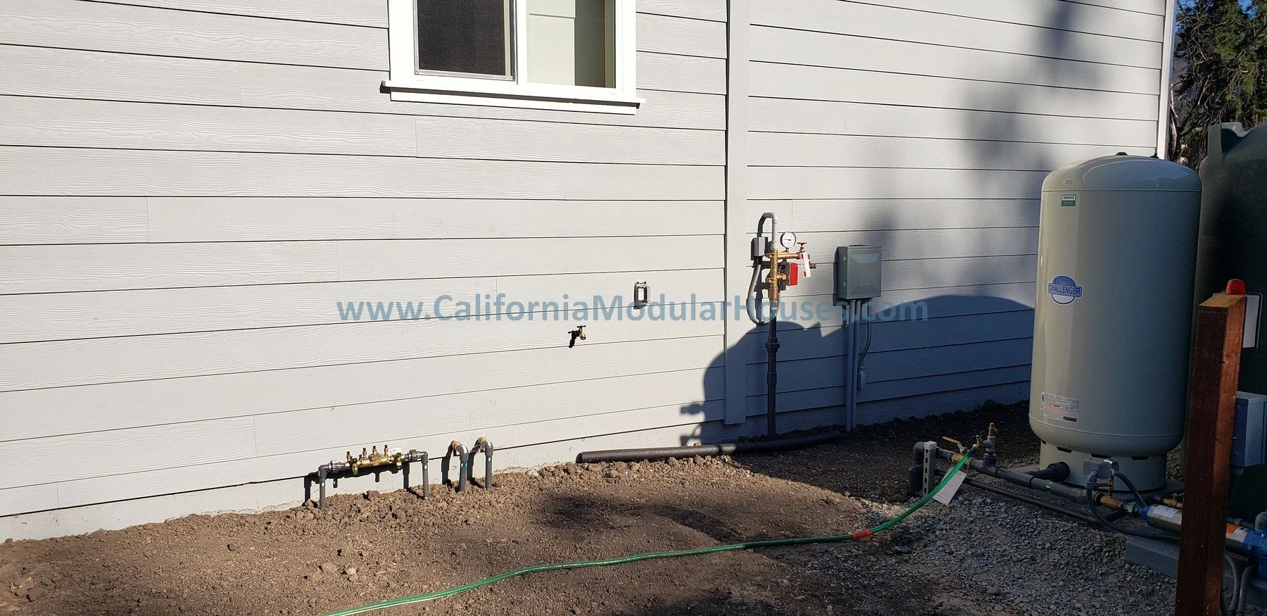 Outside view of a house with beige siding, showing a water connection system  2 bedroom, 2 bathroom modular ADU from the exterior.   Kenwood, Sonoma County, CA. 
