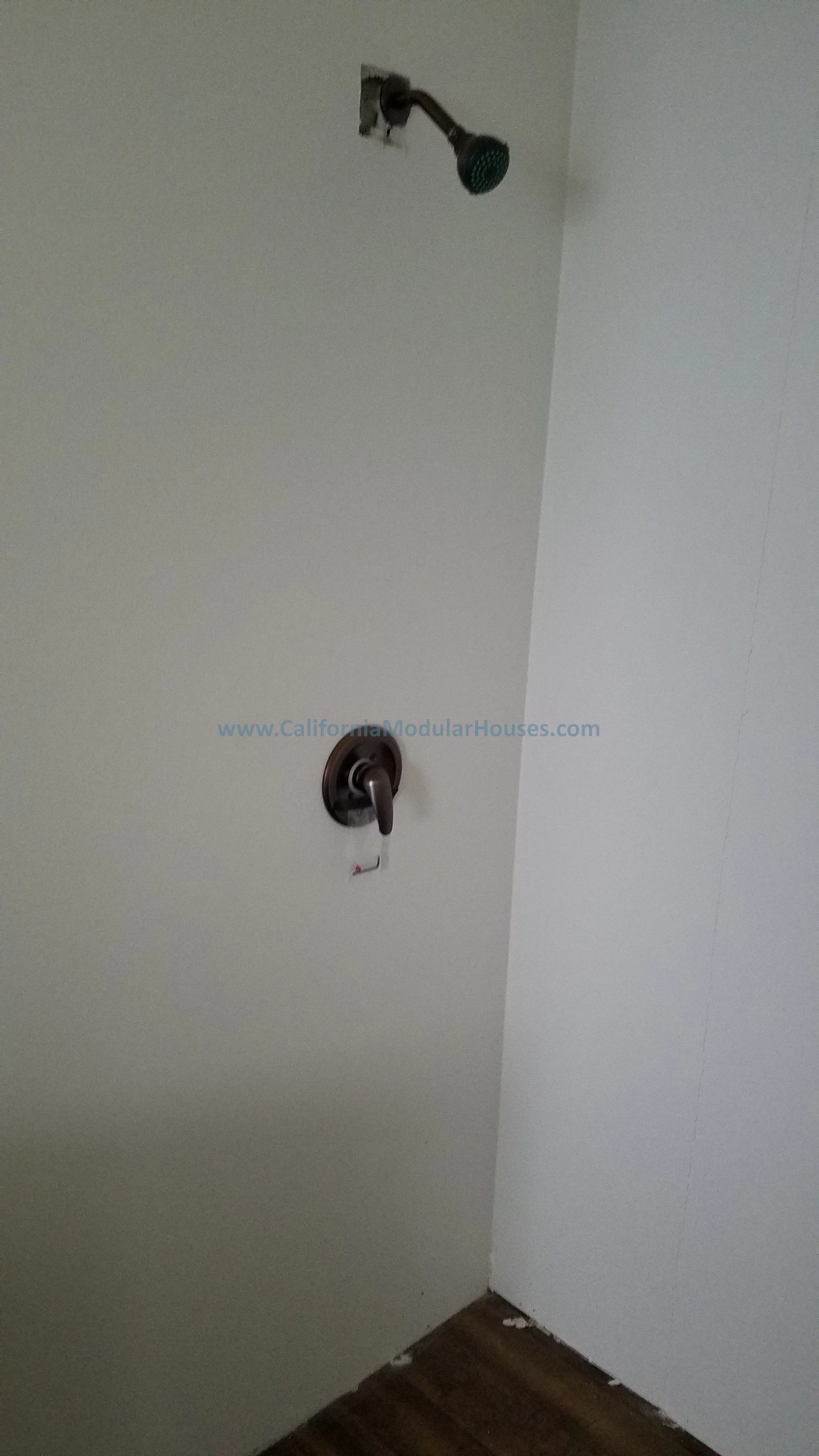 A showerhead mounted on a white ceiling and a faucet on the wall below it, with a visible water pipe connection. City of Santa Barbara, Santa Barbara County, CA.   Modular Home on a Sloped Property. California Modular.