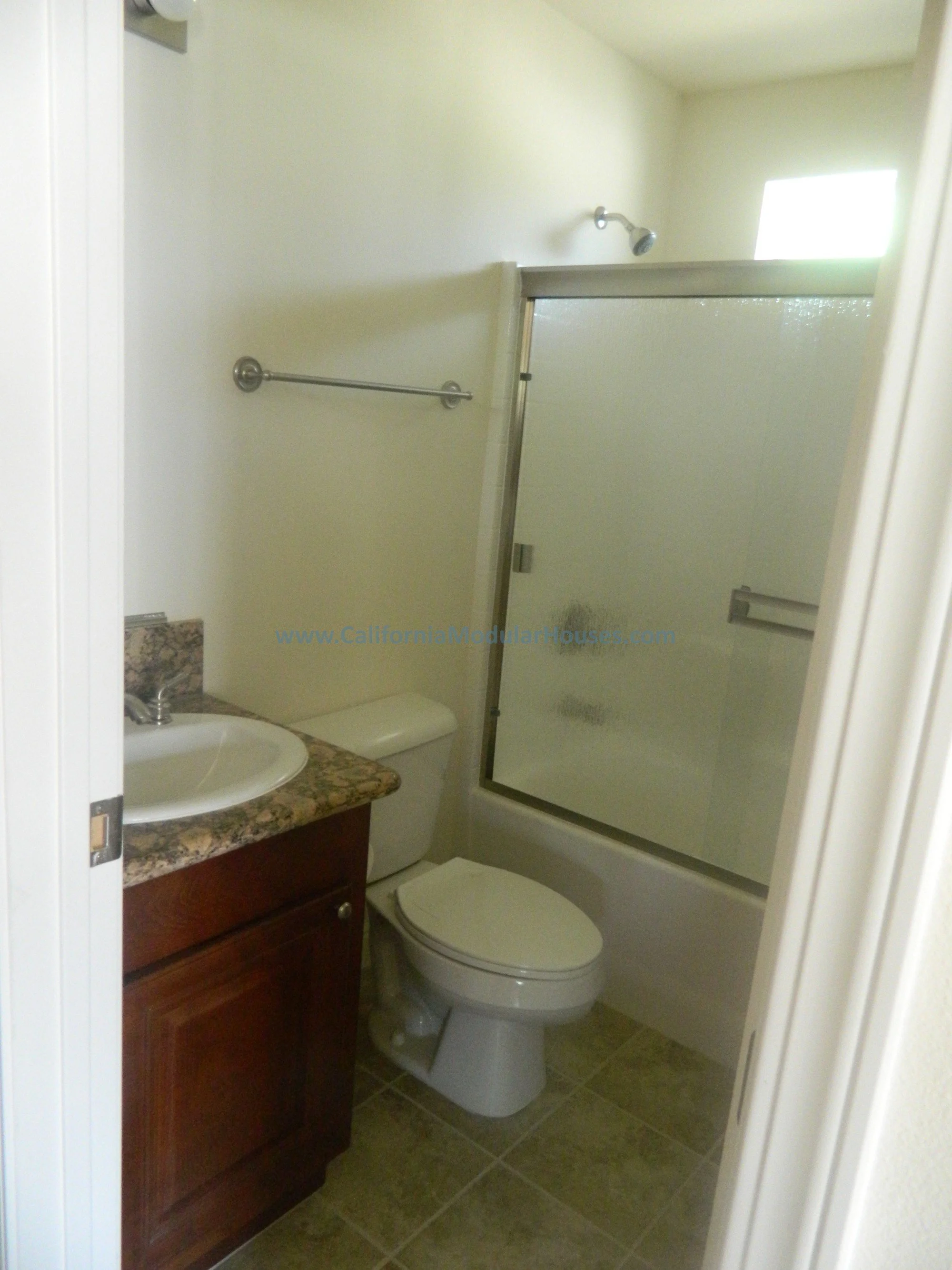Small bathroom with a sink and granite countertop, a toilet, and a glass shower door. The walls are painted light yellow and there's a small window allowing natural light.