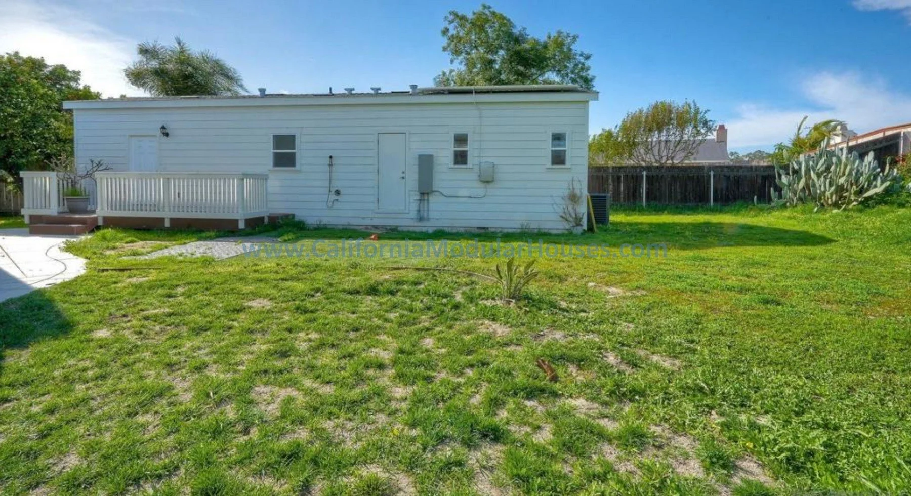 Prefab Modular ADU, Oceanside CA.  Accessory Dwelling Unit.  California Modulars.  Backyard of a white house with a small deck, green grass, and a clear blue sky.
