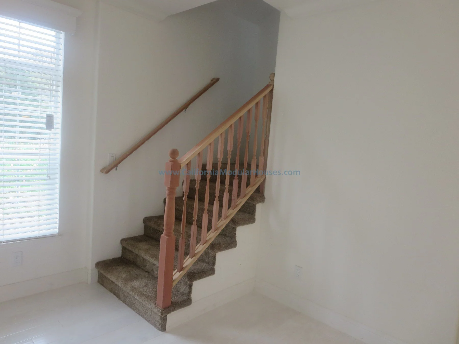 Empty room with carpeted staircase, window with blinds, and plain white walls.  Prefab.  Napa, CA.  California Modular House. California modular home.  Modulars.  