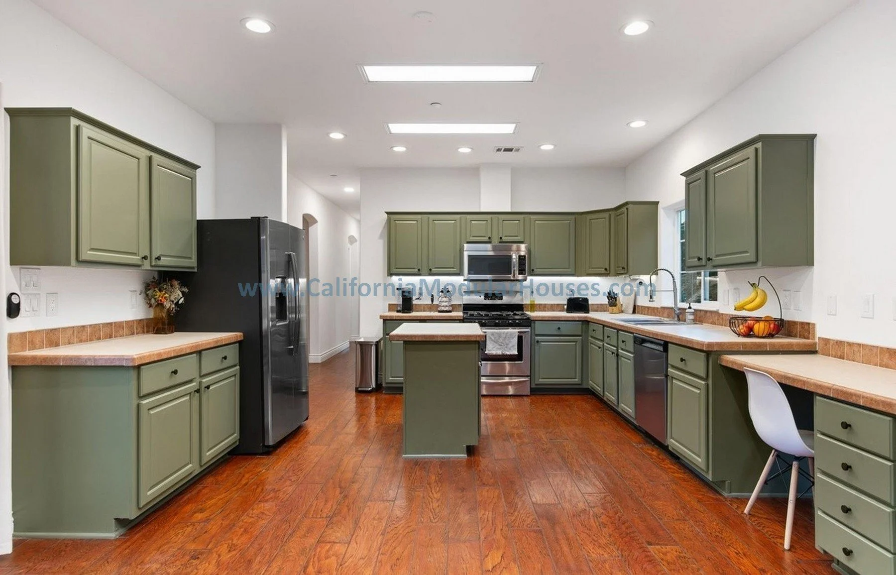Kitchen with green cabinets, stainless steel appliances, and a granite countertop with a fruit basket, bananas, and a window above the sink.