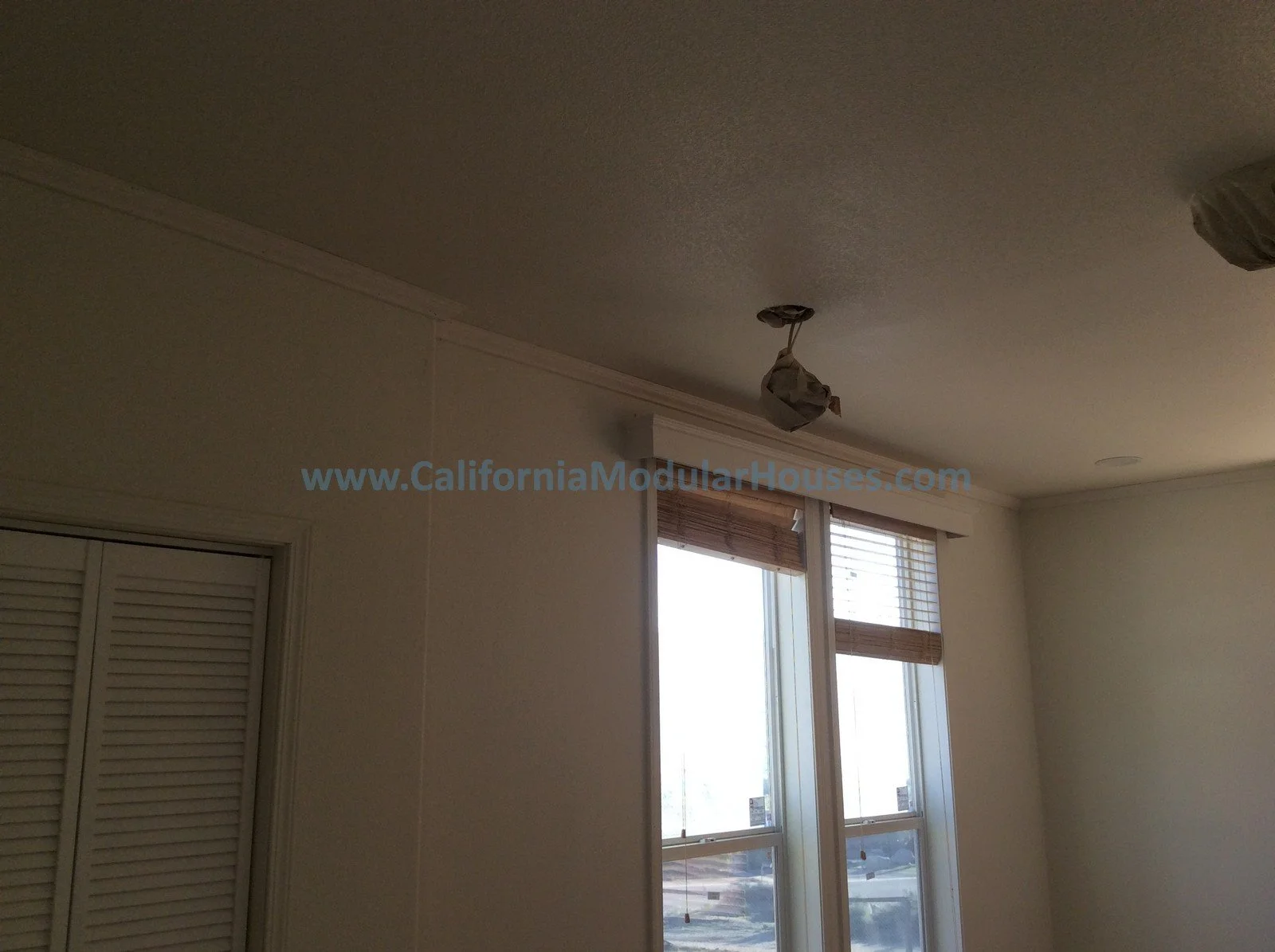 Living room with window blinds and two ceiling light fixtures covered in protective wrapping