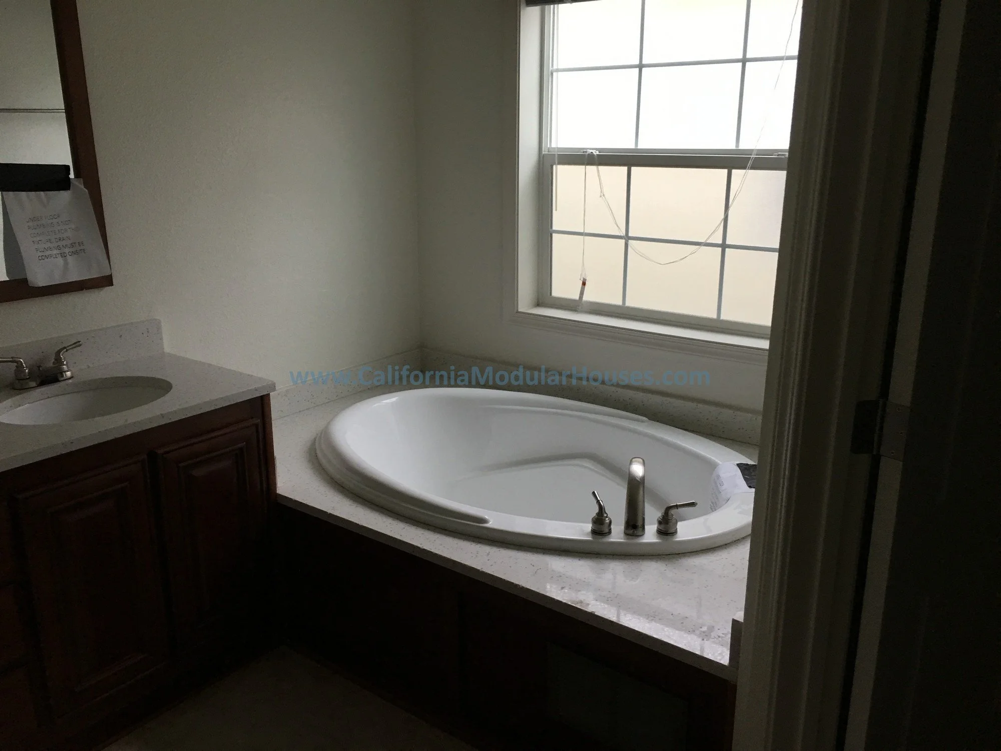 Bathroom with a white bathtub next to a window and a small sink with a wooden cabinet below.