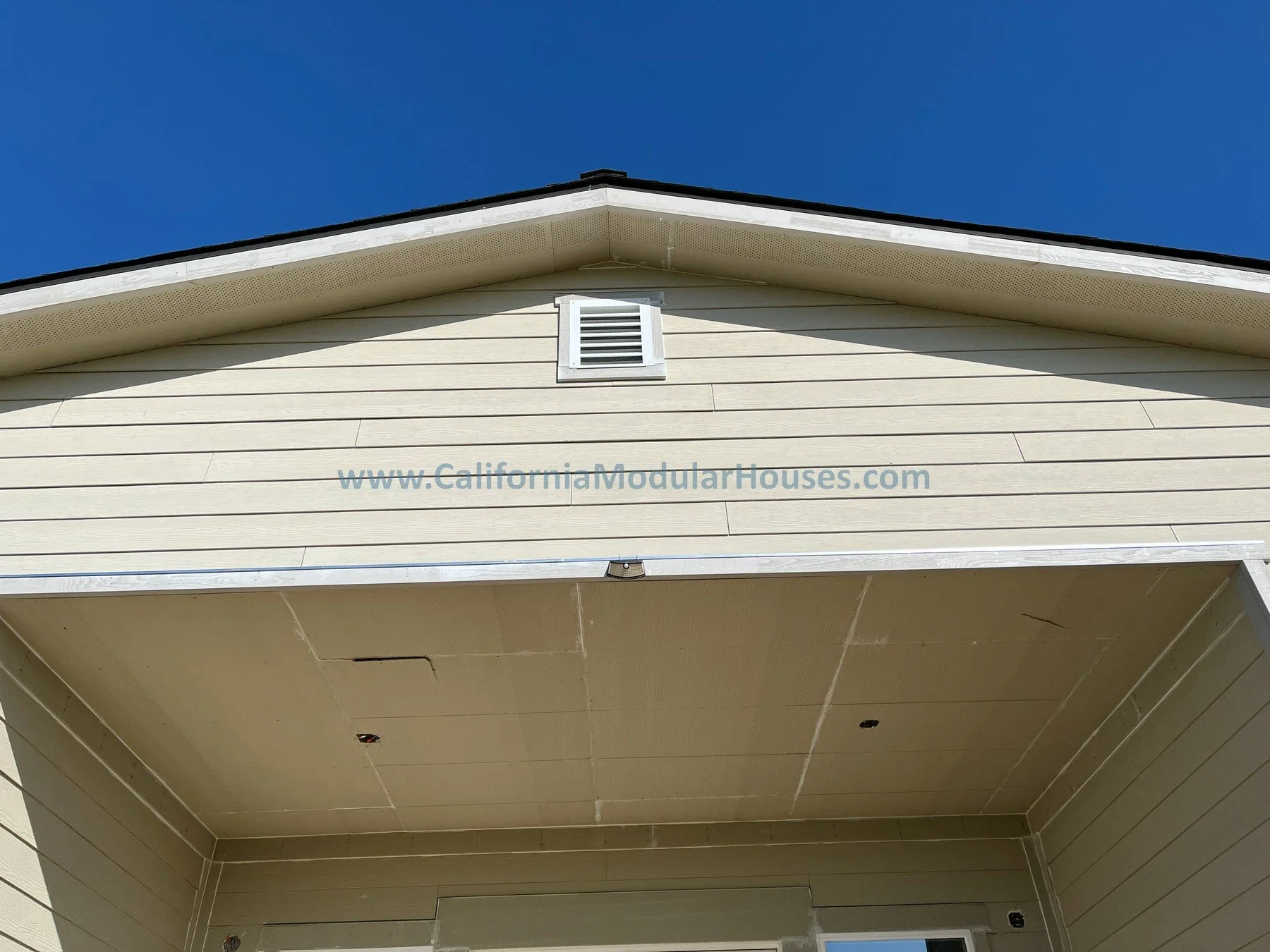 Part of a beige modular house exterior with a vent Exterior image I of a factory built home that has 3 bedrooms and 2 bathrooms California prefab modular CA