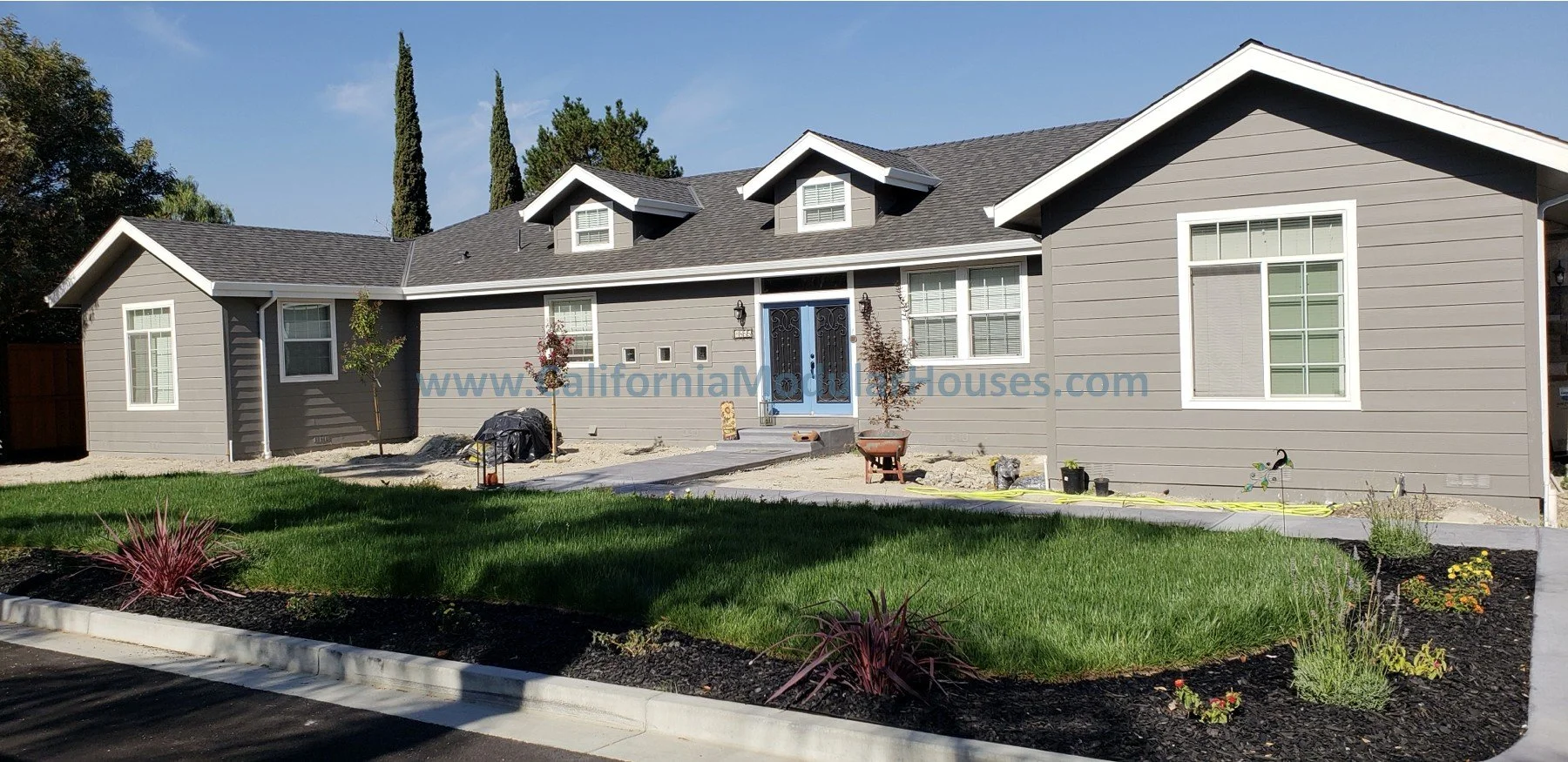 Luxury style prefab modular home, gray siding and blue door, dormer windows.