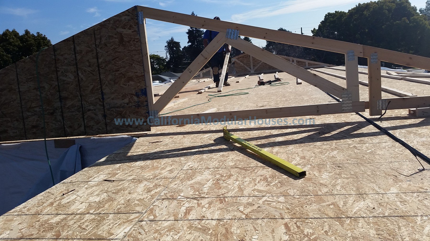 Construction site showing wooden framework and plywood for a modular house, with tools and equipment on the floor, and trees in the background. San Mateo Prefab Homes, Prefab Modular Homes California,