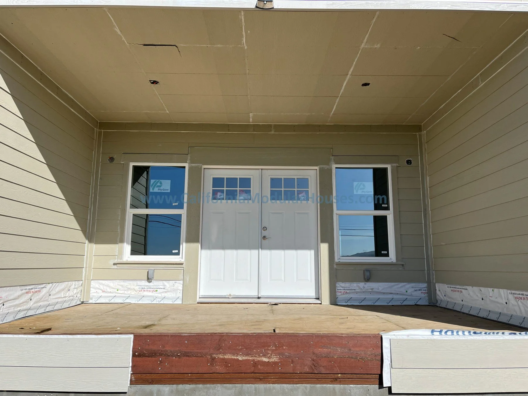 Front porch of a house under construction, with siding installed, windows in place, and a front door.  Image G exterior of a modular home that has 3 bedrooms and 2 bathrooms California modulars CA prefab
