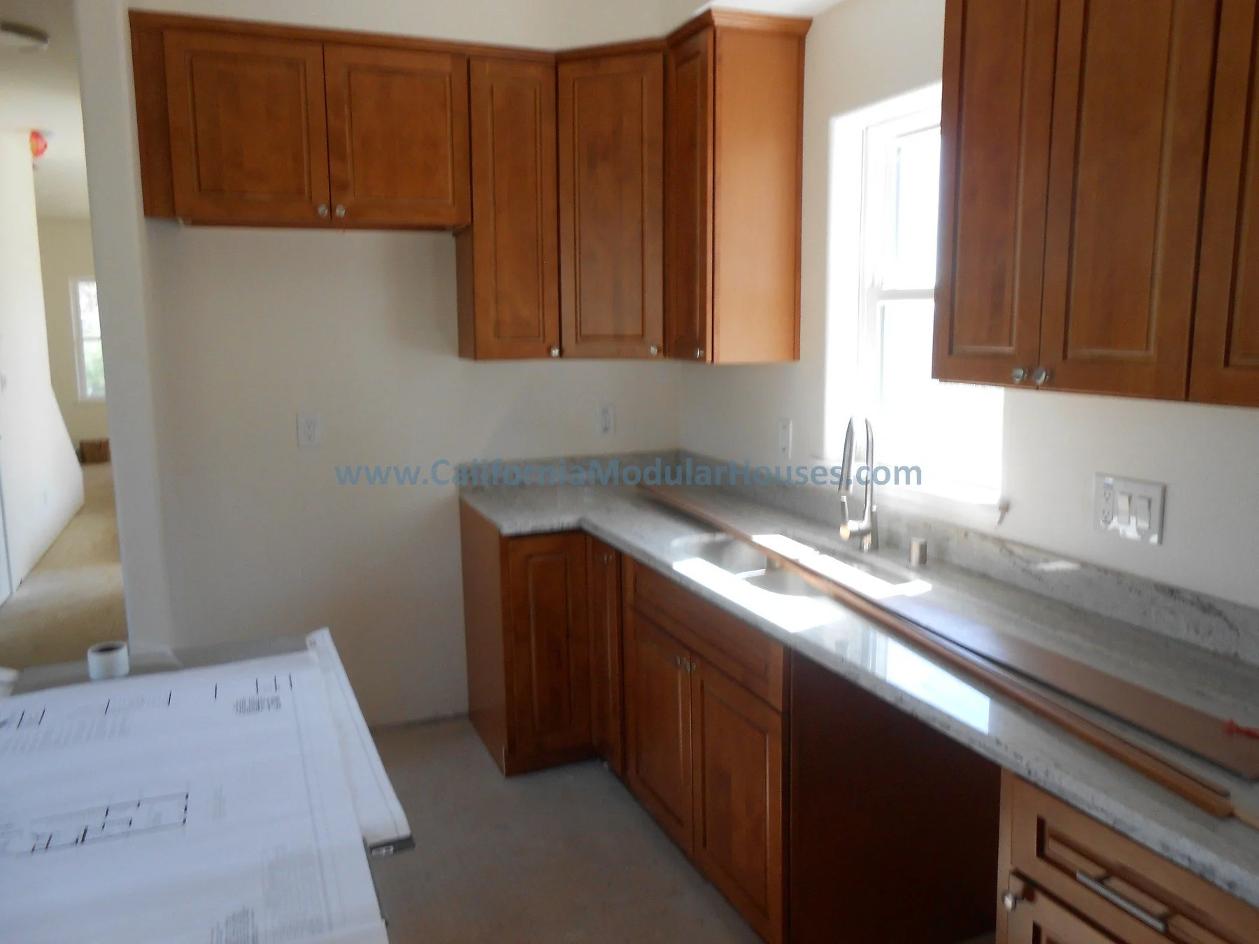 Kitchen with wooden cabinets, granite countertops, and a window above the sink.  The San Ysidro Falls model by CaliforniaModularHouses.com.  Modular Homes Northern California,Prefab Homes, Modular Homes in California,