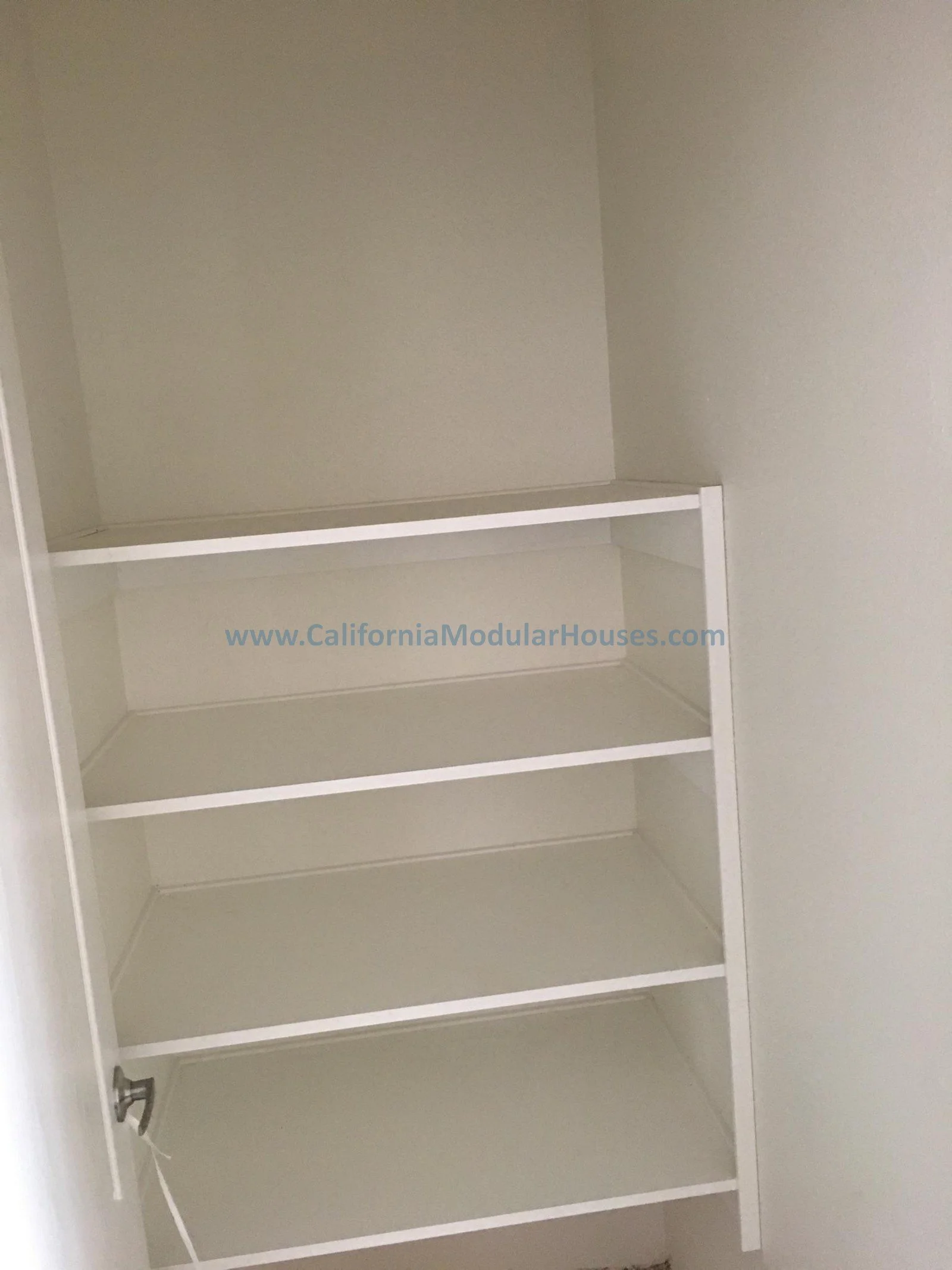 White built-in shelving with five shelves against a beige wall.  Factory Built Home.  