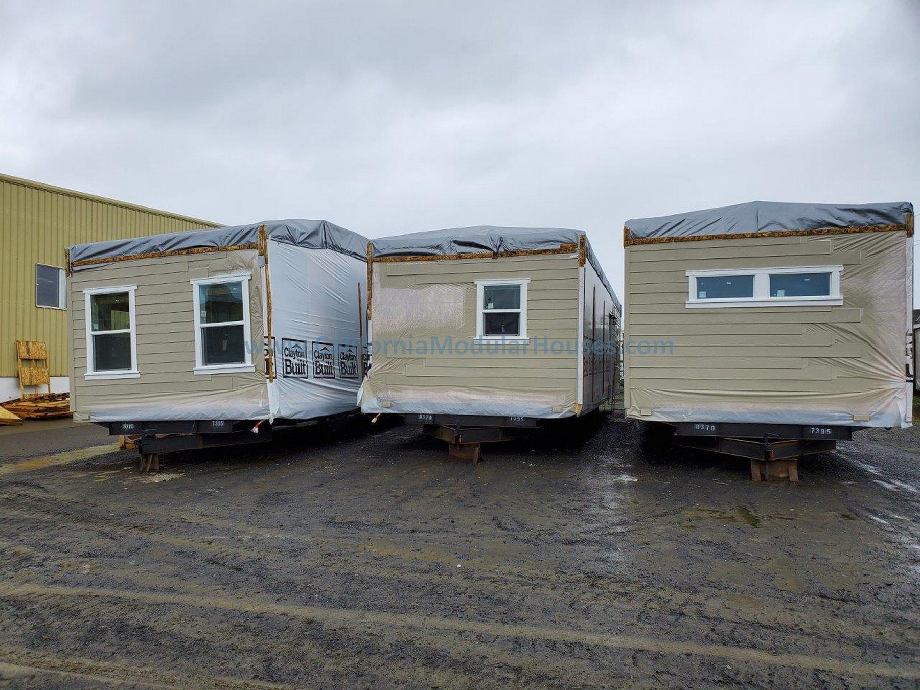 Three pre-fabricated modular home sections ready for shipping, with beige siding, multiple windows, and covered with protective plastic wrapping.  Modular Home CA, California Modular Homes, Prefab Modular Homes California,