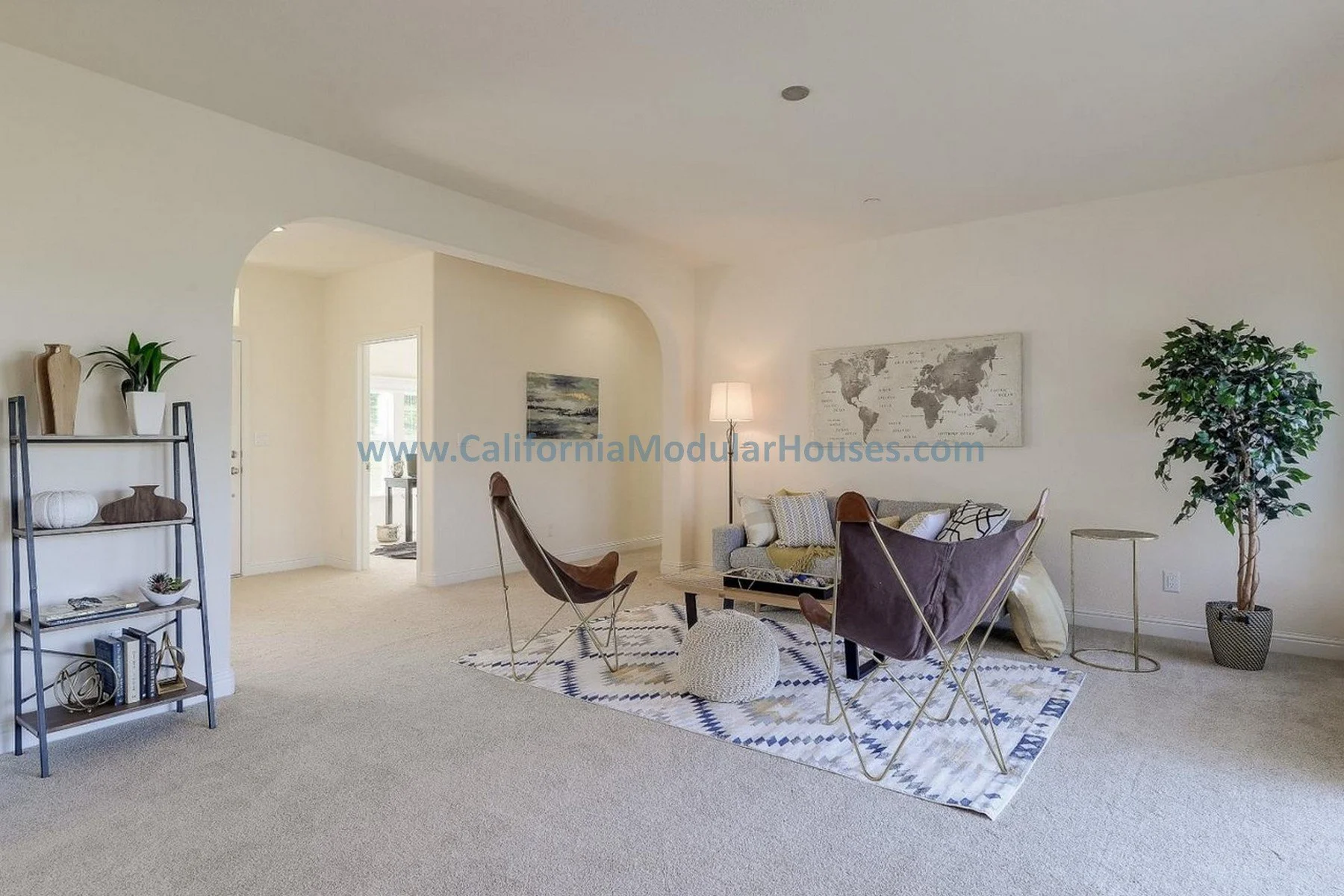 Living room with beige carpets, a patterned rug, a sofa, two modern butterfly chairs, a small table, a tall potted plant, a bookshelf, and wall art.  Bay Area Prefab Modular Home, Modular Home on a Sloped Property. 