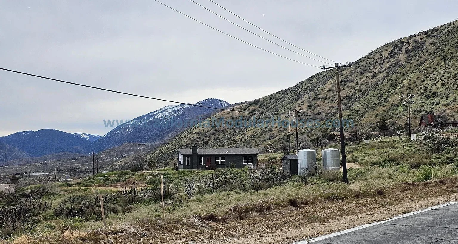 A rural landscape with mountains in the background and a modern modular home.