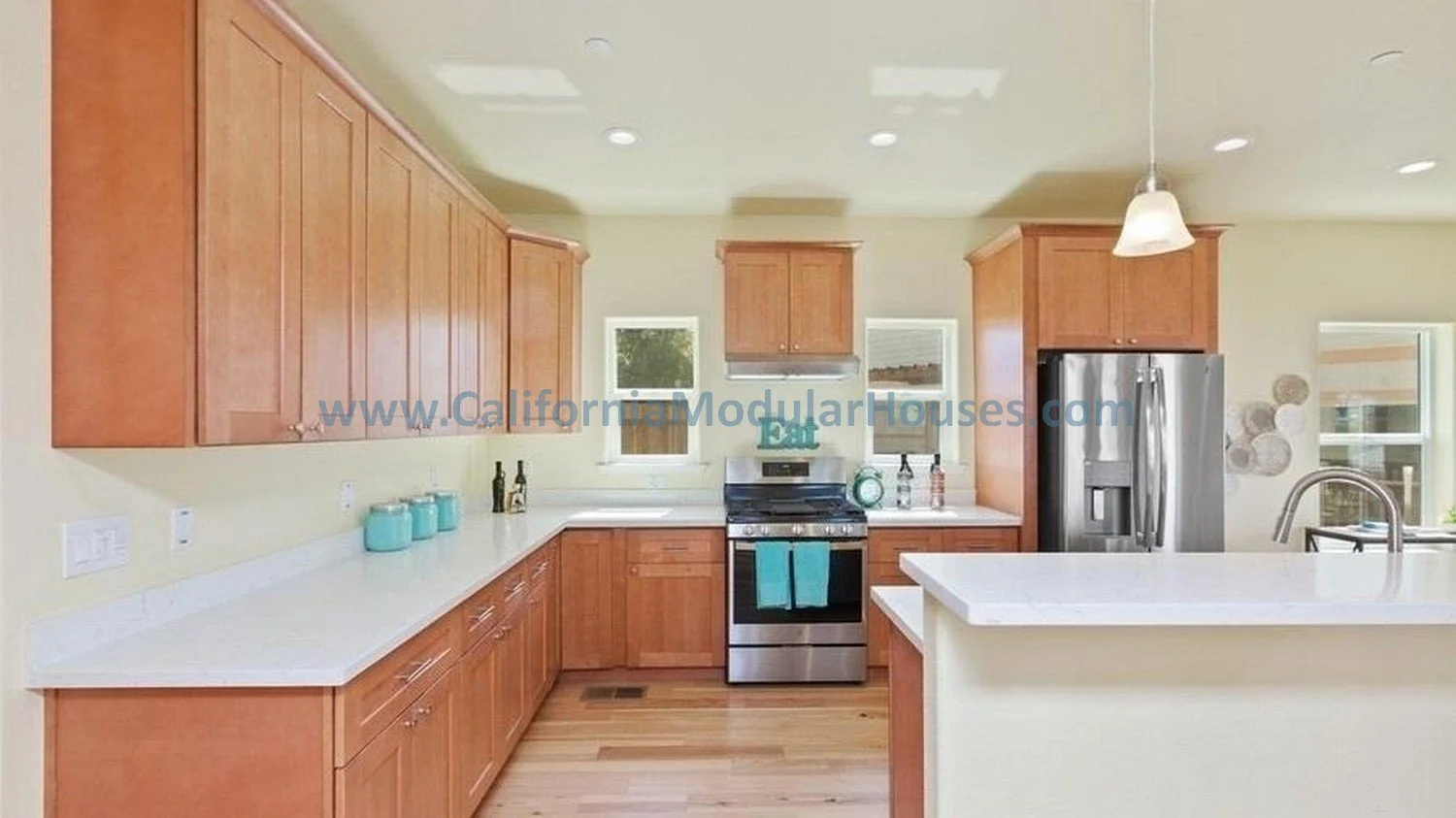 California modular home.  prefab modular CA Kitchen with wooden cabinets, white countertops, stainless steel refrigerator, gas stove, small windows, and hardwood floors.  