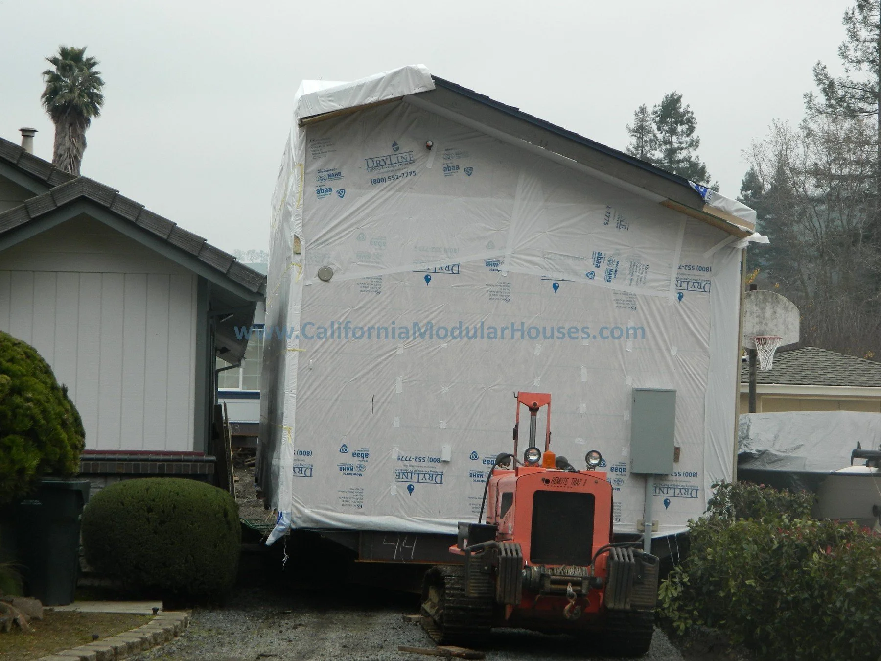 House under construction with white weatherproofing wrap on the exterior.  This shows how the delivery of a prefab modular home being delivered under tight constraints.  Modular Accessory Dwelling Unit CA