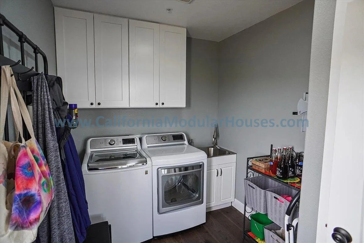 Laundry room with washer and dryer, white cabinets, small sink, and a cart with drinks, bottles, and cleaning supplies.