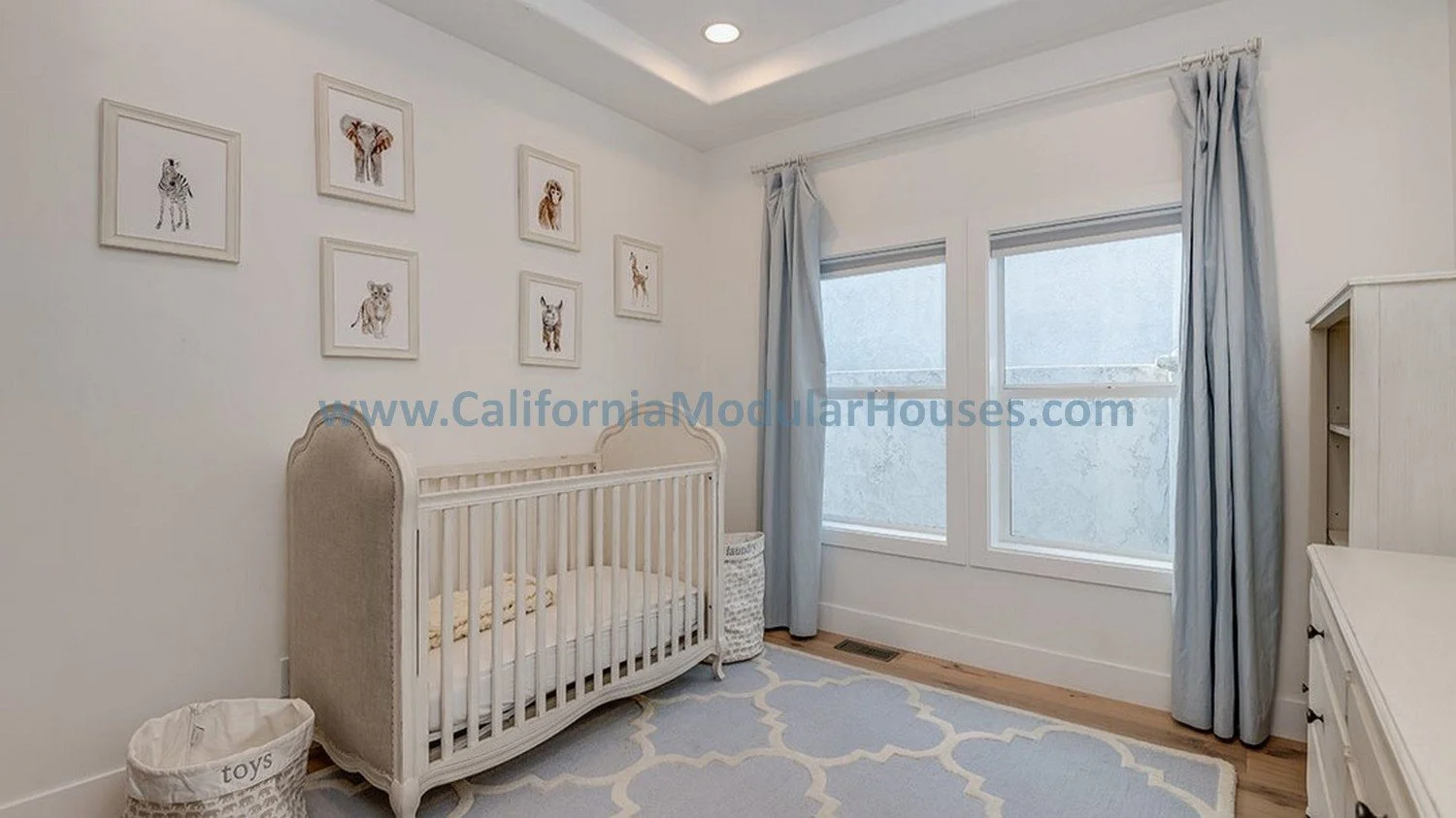 The windows with light blue curtains allow lots of natural light into this bedroom.  The home has tray ceilings, recessed canned lights and fire sprinklers.  Modular home.  