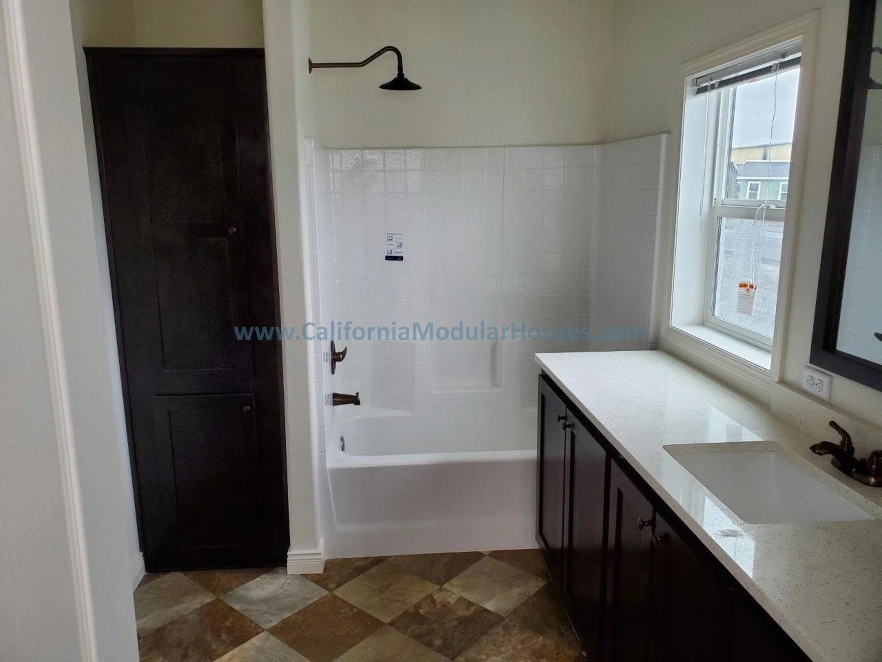 Bathroom with dark cabinetry, a bathtub with a showerhead, a window with a countertop below, and a tiled floor. City of Santa Barbara, Santa Barbara County, CA.  Modular Home on a Sloped Property. Two-Story Modular Home.