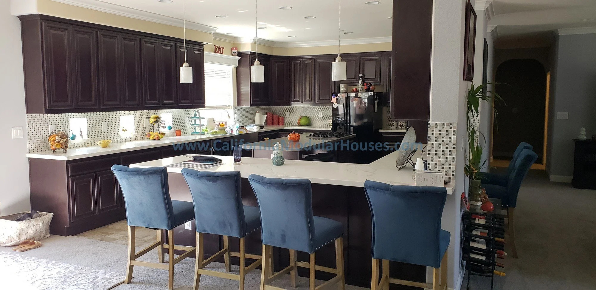 The Modular "Hollywood Series" of homes is to have a large kitchen where the living room is together with the kitchen for entertaining and family living.  This features hardwood cabinets & hard surface counters with a barstool seating area. 