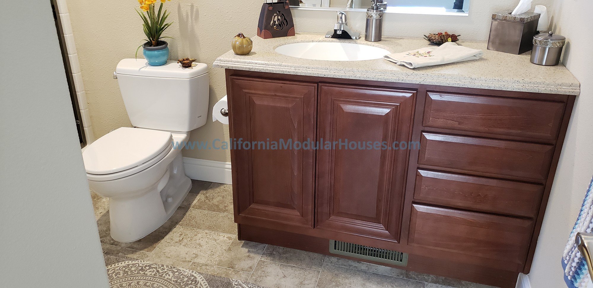 In this factory built home you have an on-site tiled floor.  The cabinets are all wood faces and doors, with drawers.  There is a hard surface countertop with a mirror above it and a nice space for the water closet.  