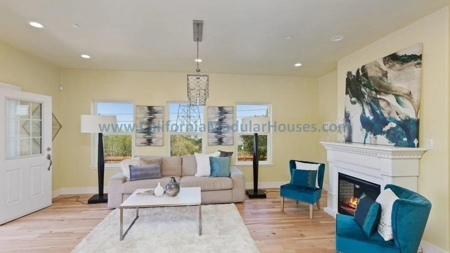 Living room with beige sofa, blue armchair, fireplace, artwork, window view, and hardwood floors.  Modular home upon completion.  Modules.  California.  San Francisco Bay Area