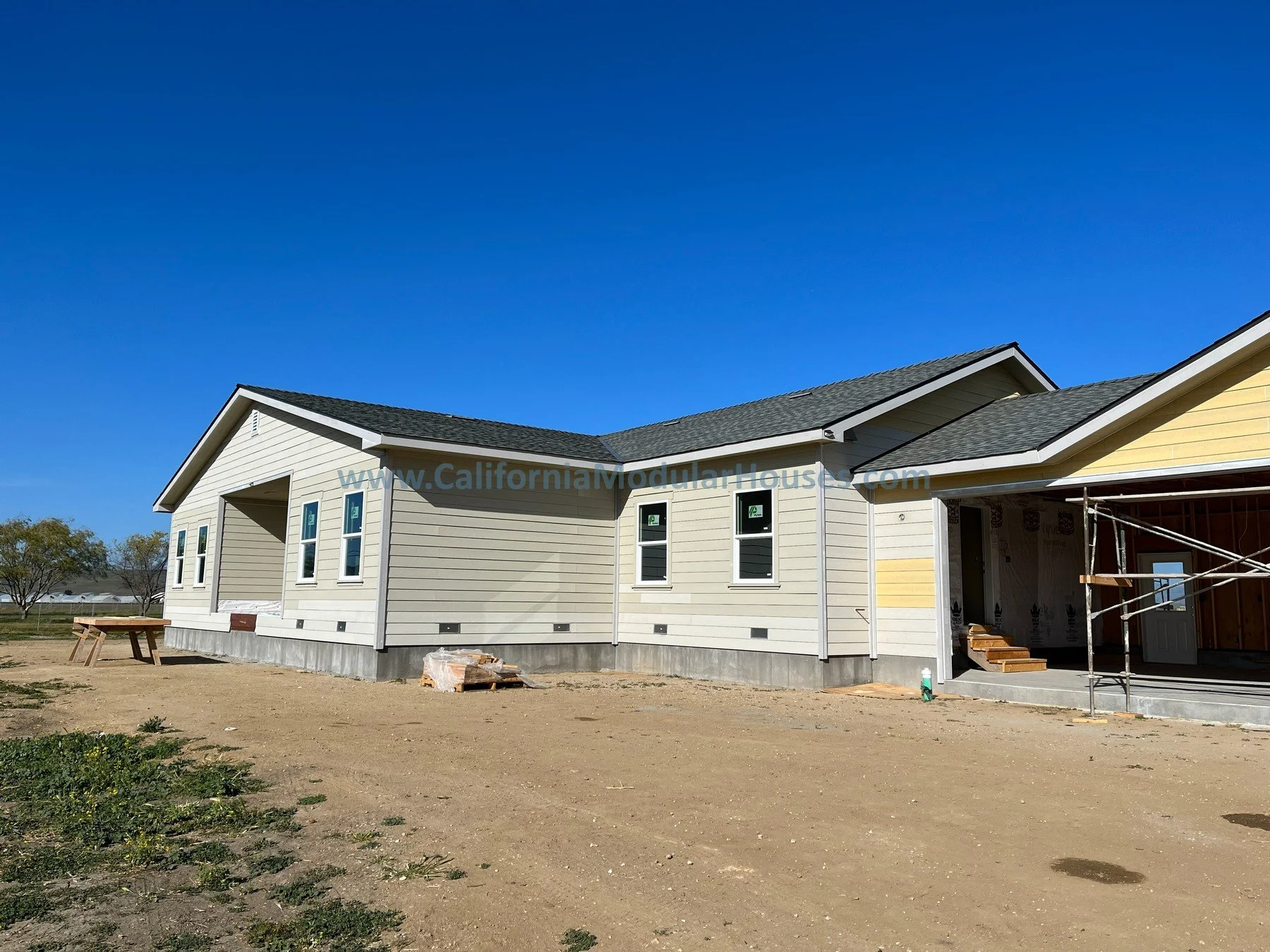 Newly constructed house with beige siding, dark grey shingles, and a front porch under construction Exterior image G of a factory built home that has 3 bedrooms and 2 bathrooms California prefab modular CA