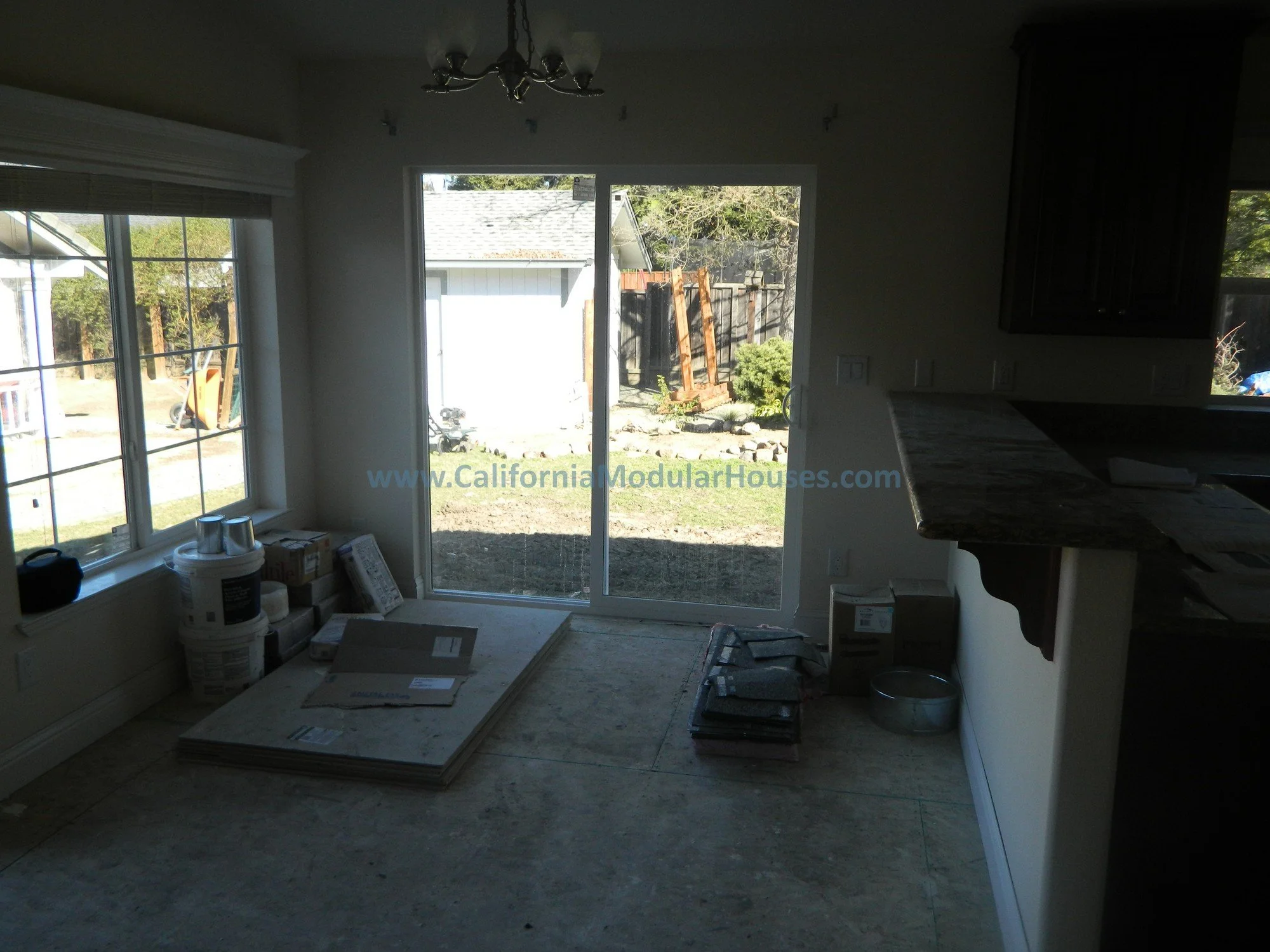 Interior of a house under construction with a sliding glass door leading to the backyard, construction materials on the floor, and a window on the left side.