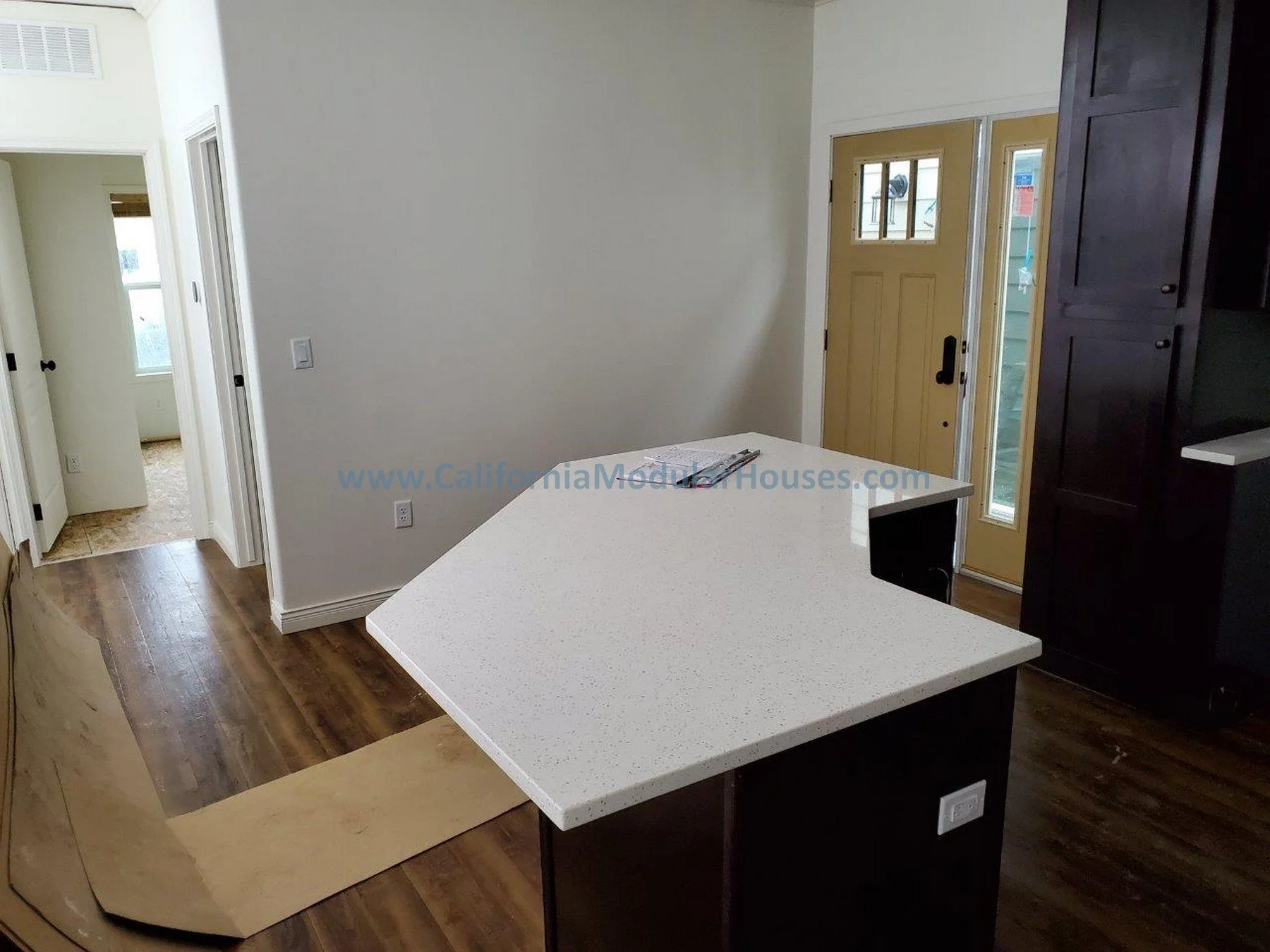 Kitchen with white countertop island, dark cabinets, and front door with window and sidelight. Wooden flooring.  City of Santa Barbara, Santa Barbara County, CA.   Modular Home on a Sloped Property.  Two-Story Modular Home.