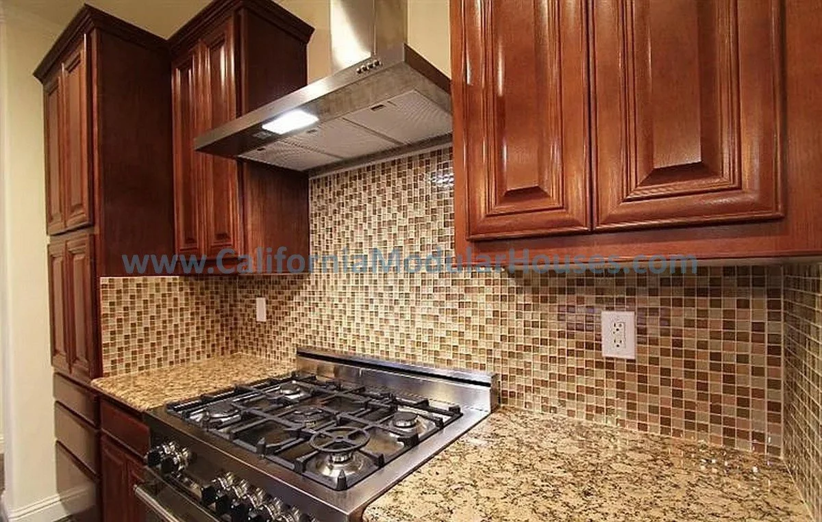 Kitchen with wooden cabinets, stainless steel gas stove, granite countertops, and mosaic tile backsplash.