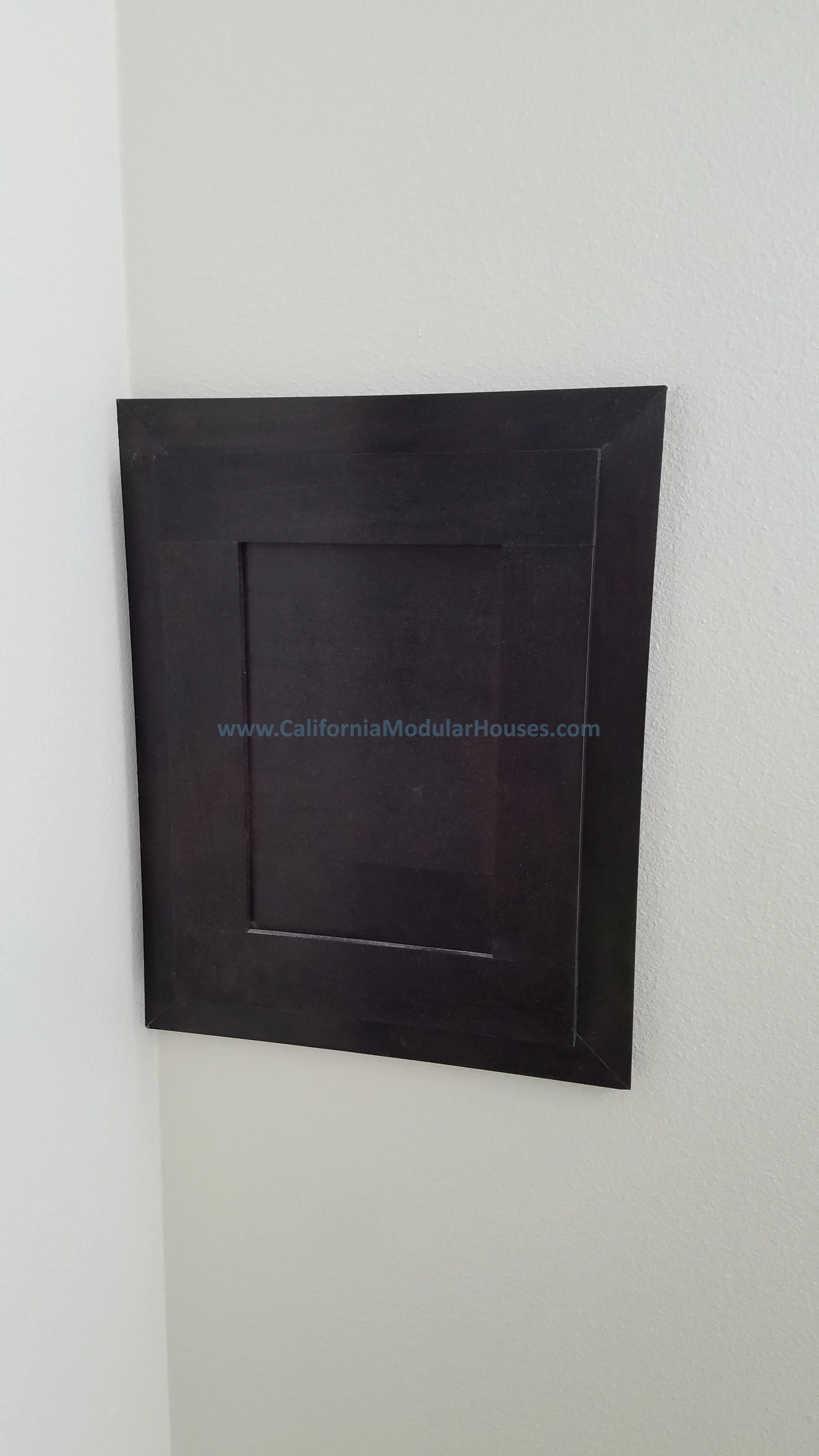 A black framed panel mounted on a white wall by California Modular Houses in the center.  City of Santa Barbara, Santa Barbara County, CA.  Modular Home on a Sloped Property. 