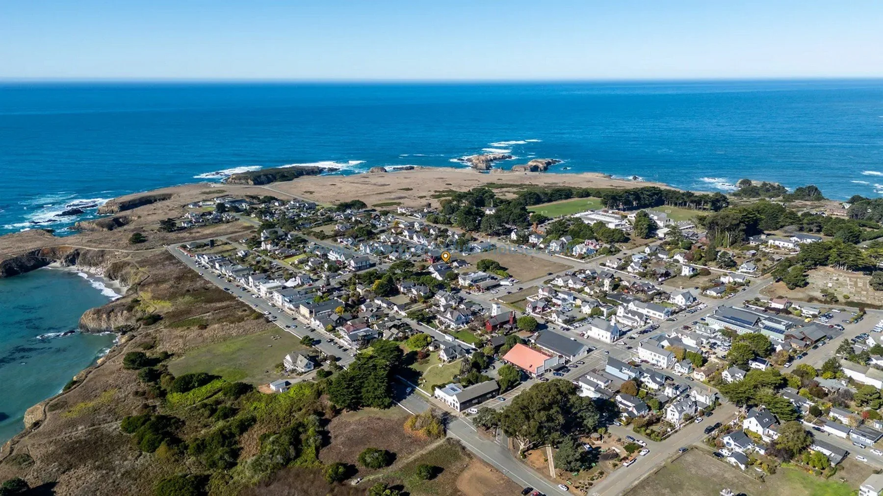 Aerial view of a coastal town with beaches, houses, and streets extending along the shoreline and into the land, with the ocean in the background.  California prefab modular home for Mendocino CA.  