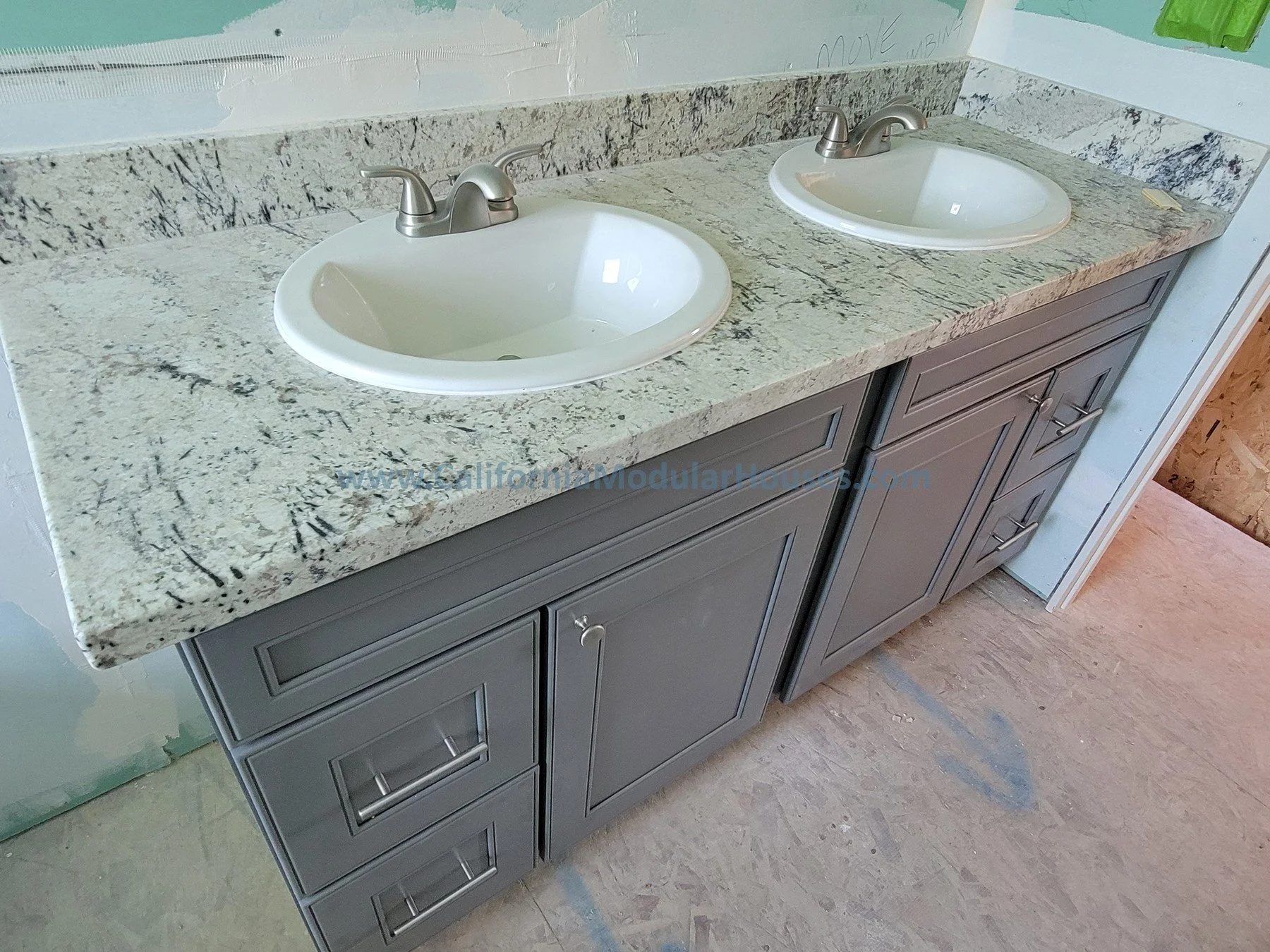Double bathroom vanity with granite countertop and two oval sinks in a partially finished bathroom.