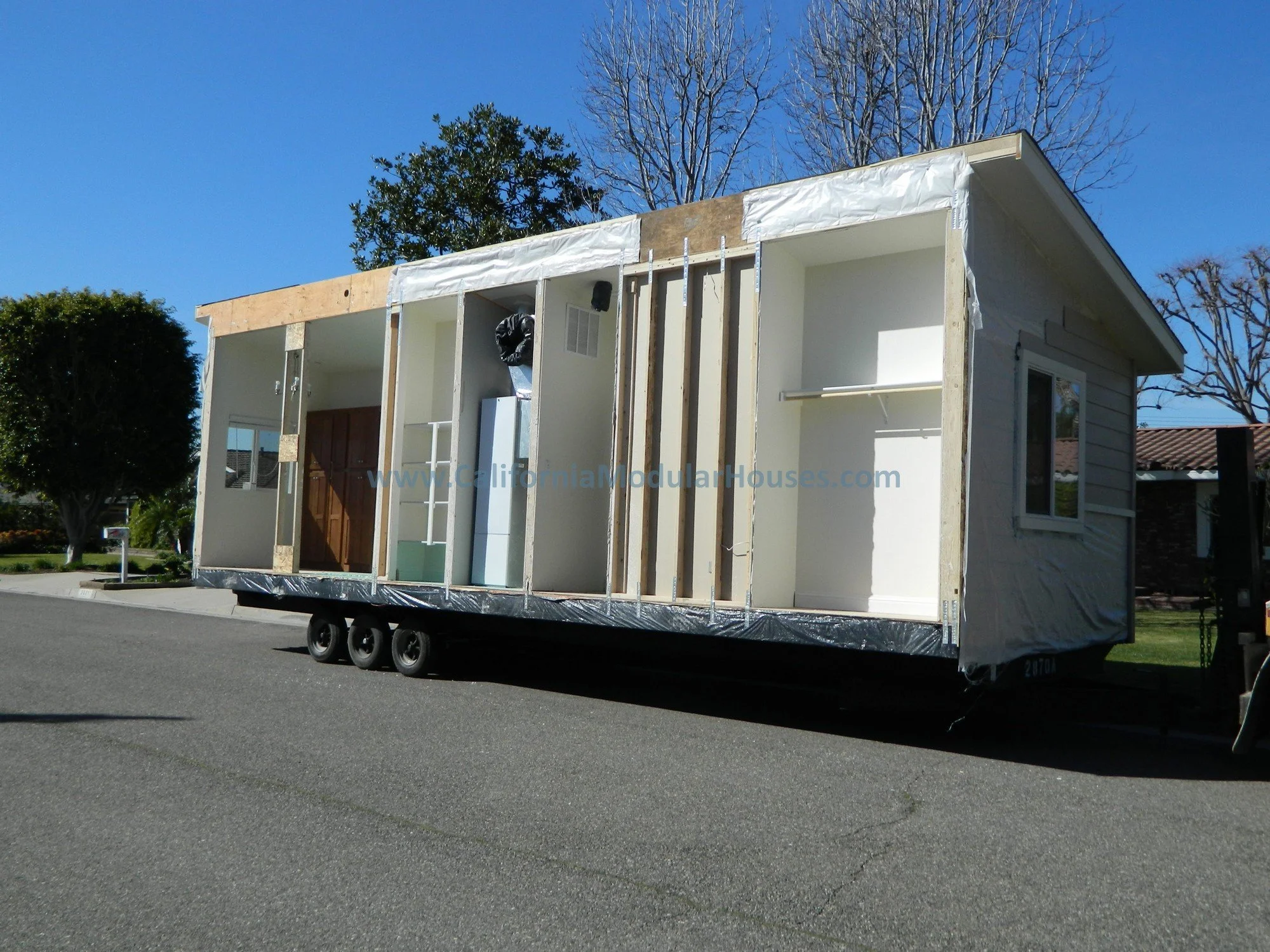 An in-law backyard unit under construction ready for transportation to the property, showing interior walls, windows, and wall framing on a sunny day.