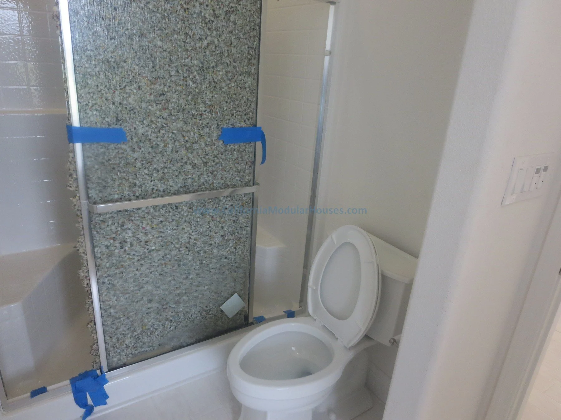 Prefab.  Napa, CA.  California Modular House. California modular home.  Modulars.  A bathroom with a toilet in front of a shower with a glass door and a granite wall, in an unfinished or under-construction state.