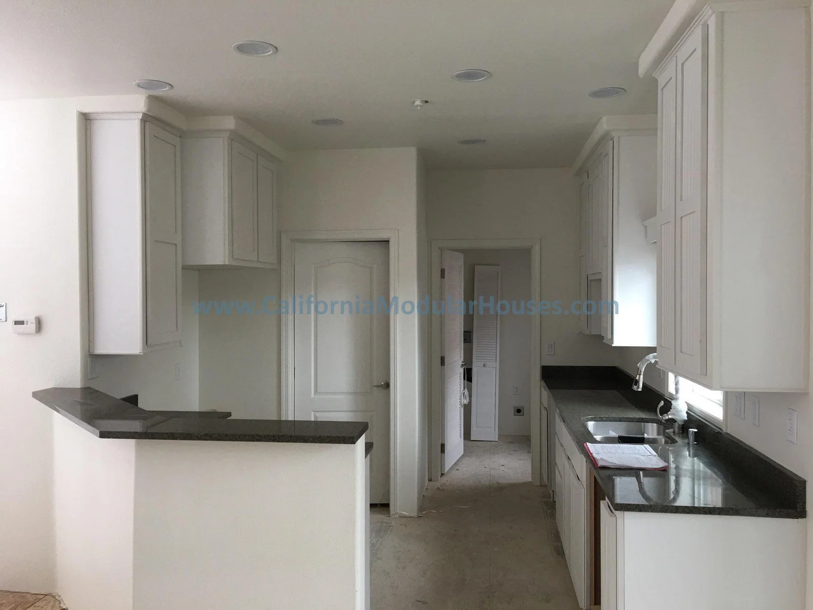 Brand new kitchen with white wood cabinets, black quartz countertops, and a sink under a view window.  New Single Family Residence.  