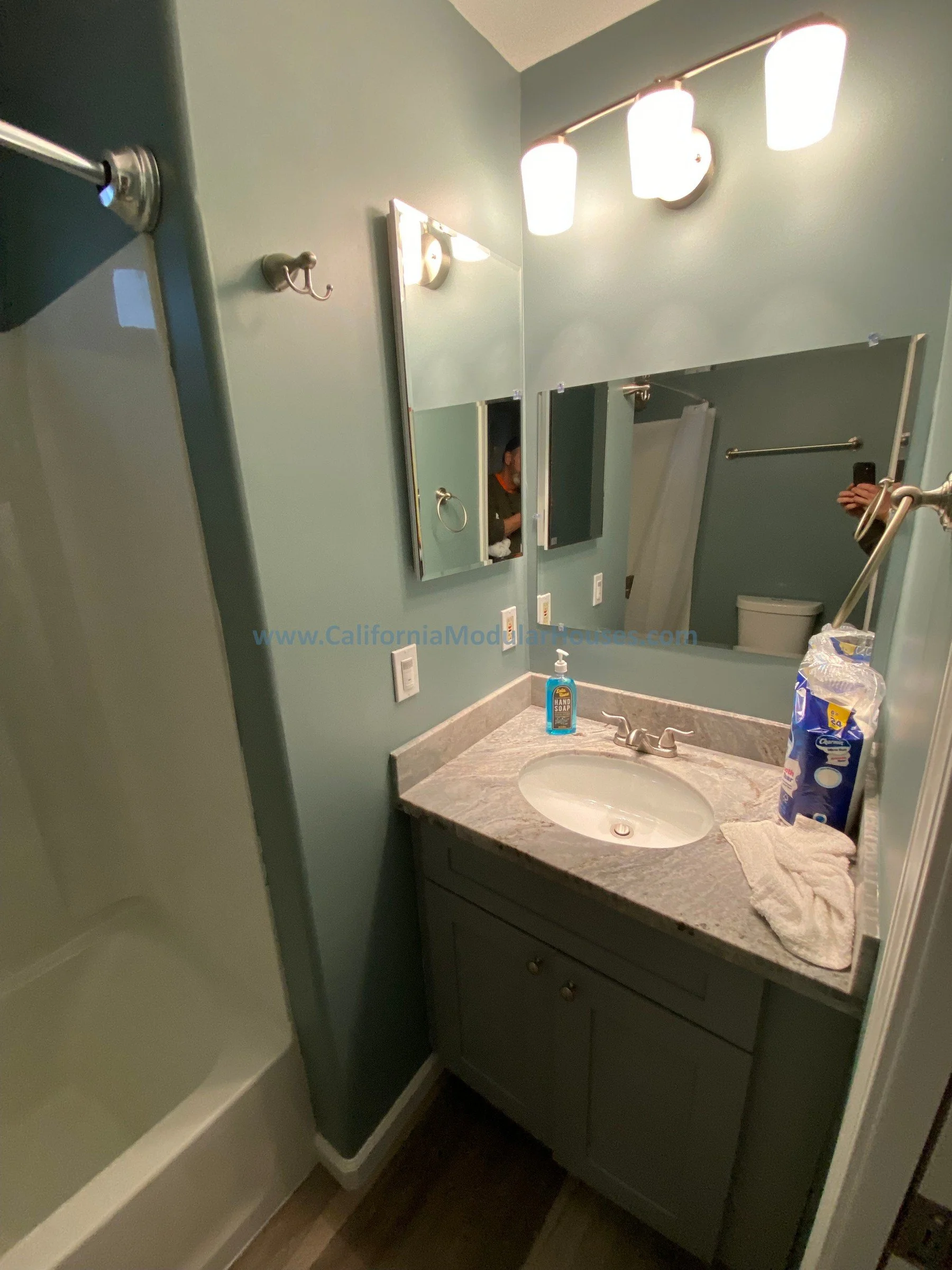 A small bathroom with a blue wall, a mirror above the sink, a vanity with a quartz countertop Modular Accessory Dwelling Unit Modular Contra Costa County, CA.  