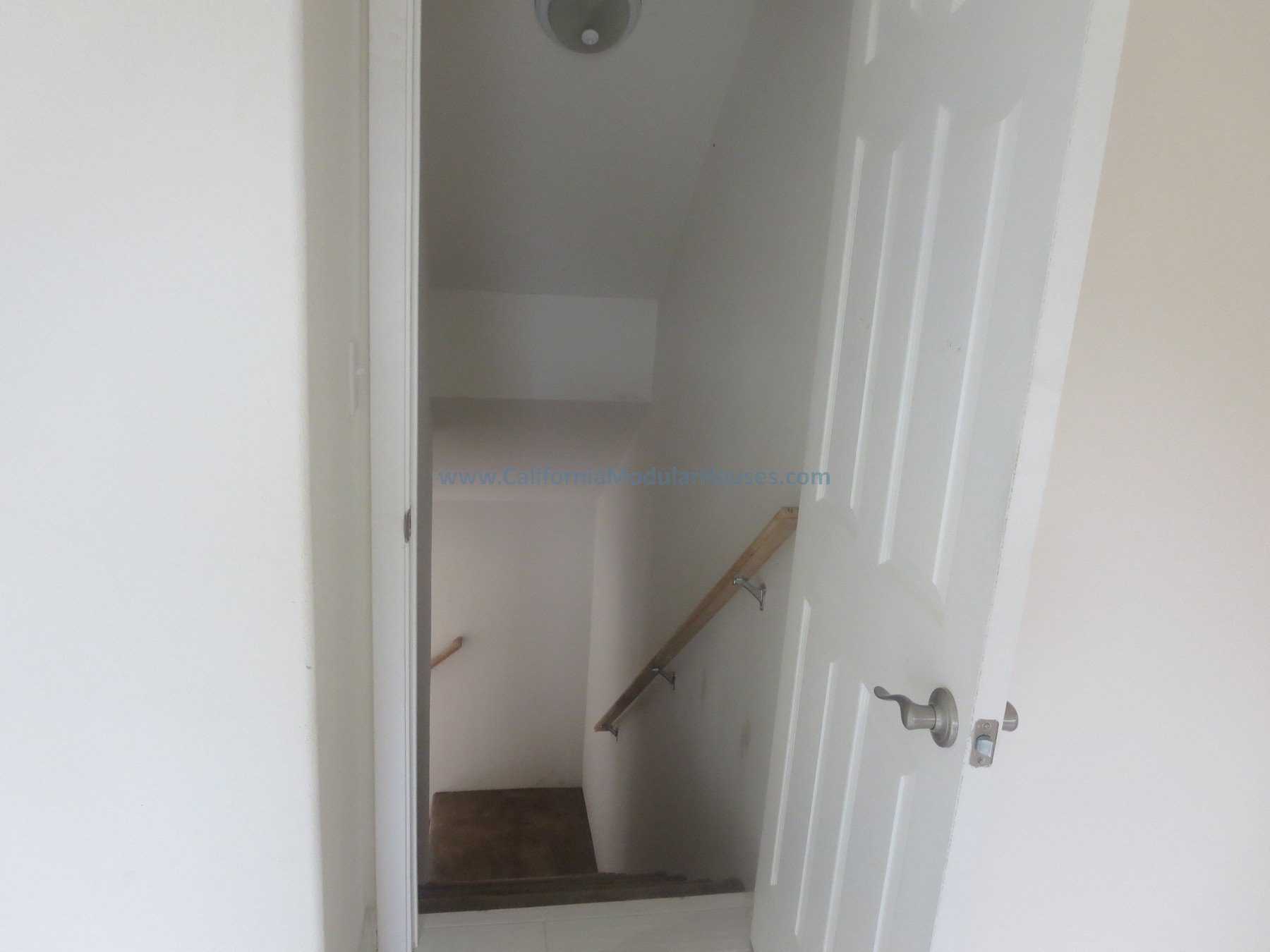 Napa County, CA. Modular. Pre-fab Modular.  Cape Cod.  Modulars for Napa.  Open white door revealing a staircase with a wooden handrail leading down in a small, white-walled room.