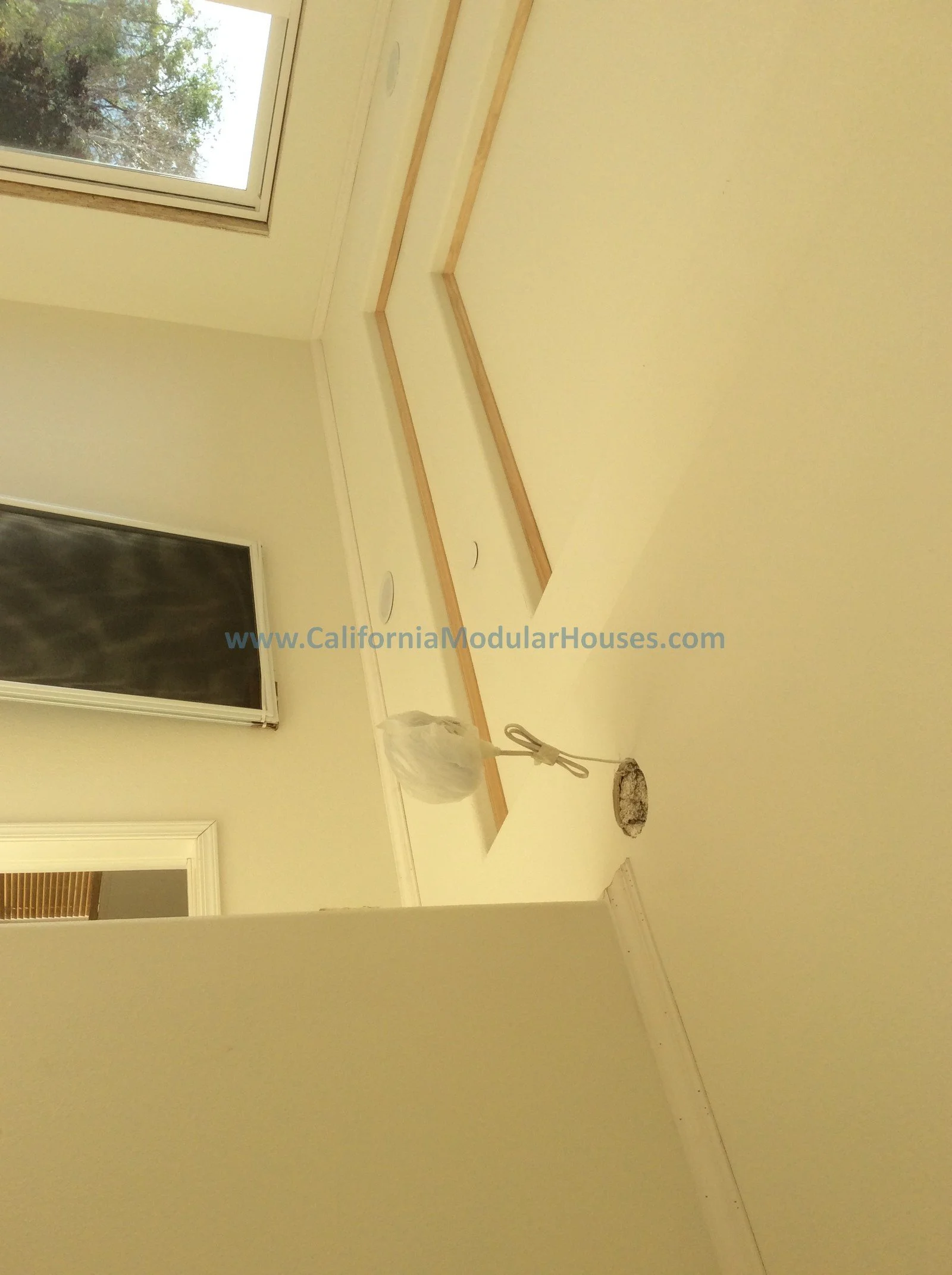 Beautifully designed interior wall with inset corner shelf, painted in light cream color, with two ceiling-mounted round vents and a window showing trees outside.