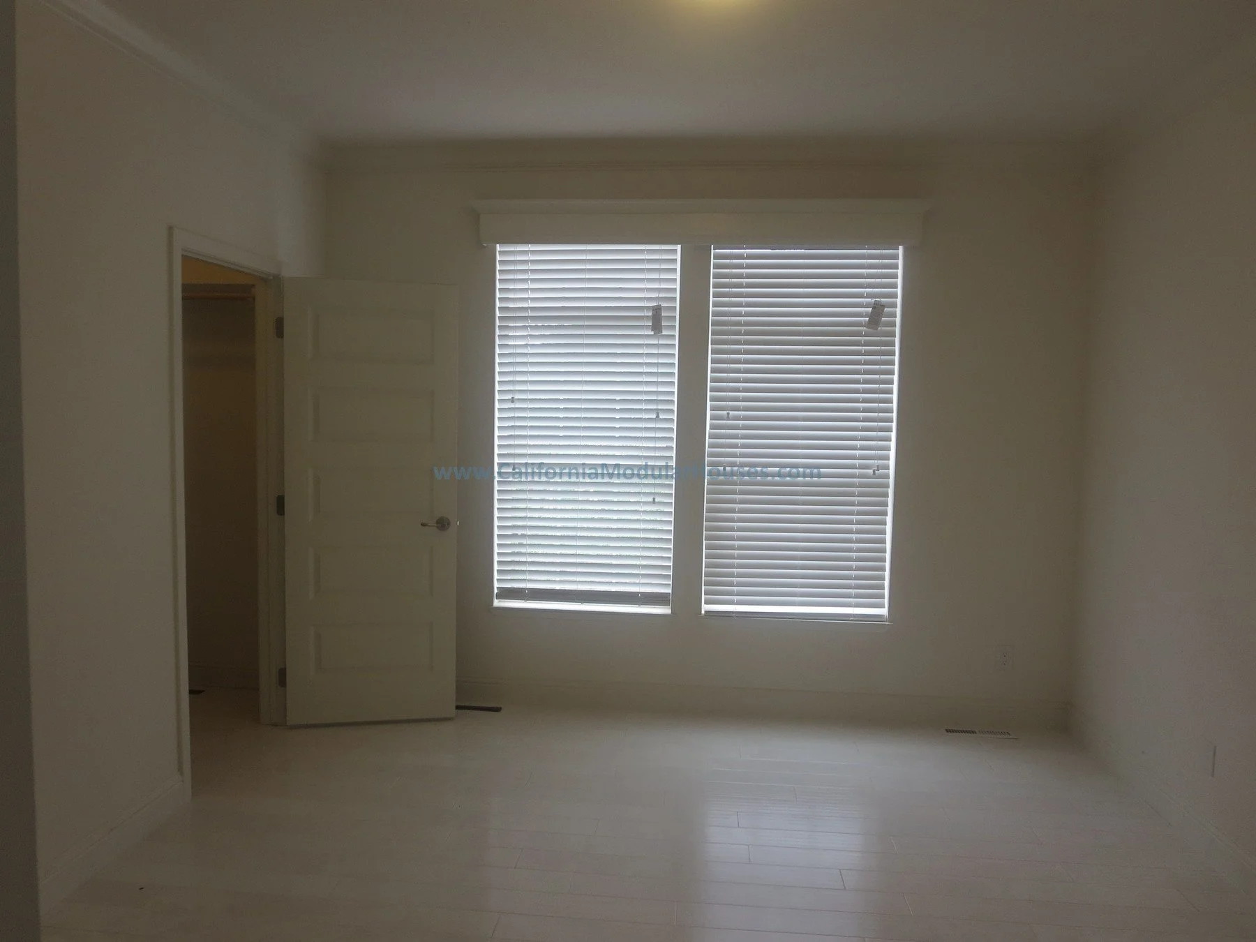 Empty beige bedroom with closed closet door and large windows with blinds, natural light streaming in.   California modular home.   Unfinished attic.  New prefab modular house in Napa, CA.  