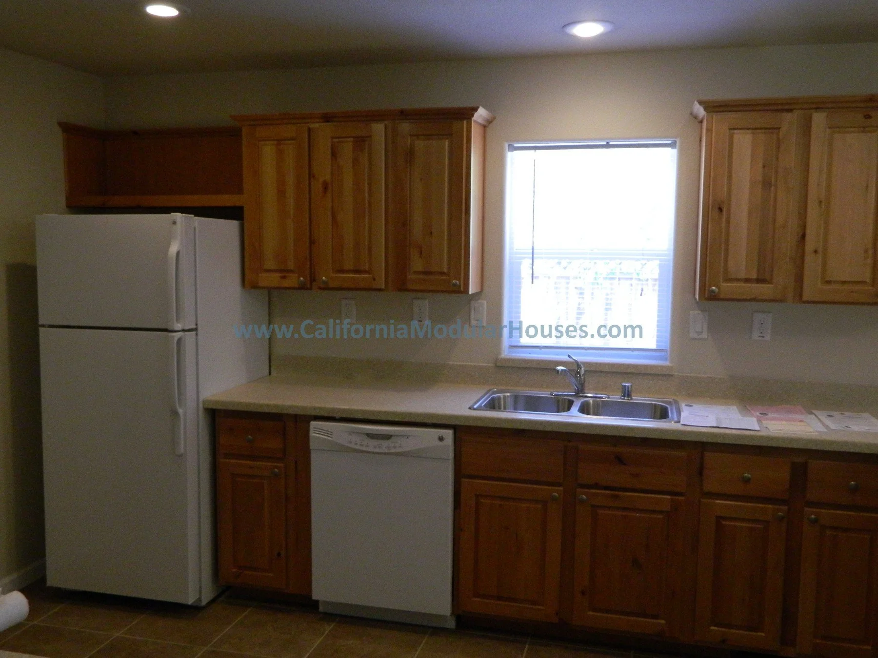 Kitchen with wooden cabinets, white refrigerator, dishwasher, double sink, and a window above the sink.