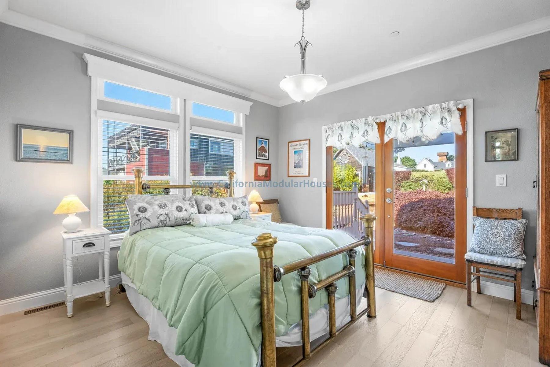 A cozy bedroom. Features large windows and a sliding glass door leading to a balcony, with various framed pictures on the walls and a wooden chair near the door.  California modular.  Prefab CA.  Mendocino.