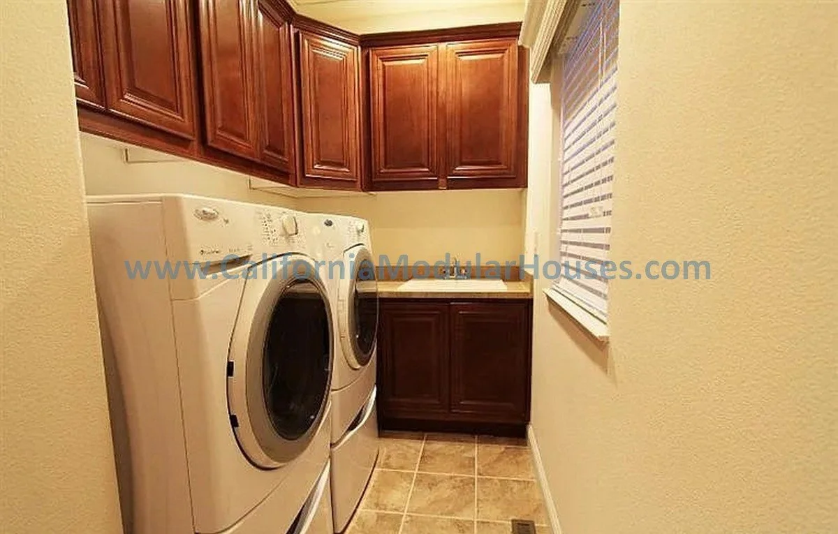 Laundry room with front-loading washer and dryer, dark wood cabinets, a small sink, beige walls, and a window with blinds.