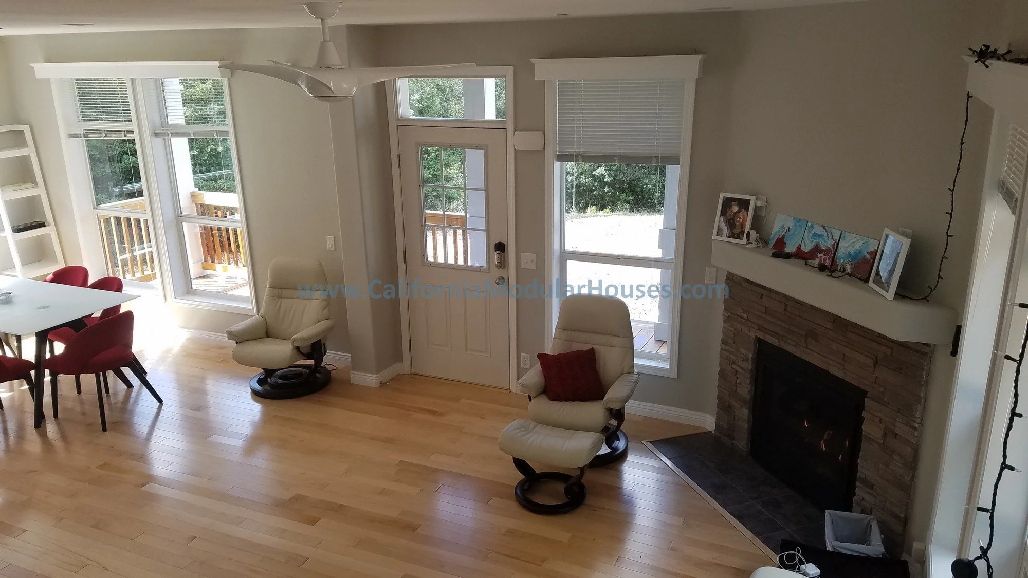 Interior of a living room with hardwood flooring, a fireplace with a stone surround, a great view from the stairs looking down into the beautiful living room of this Factory Built Housing home built in Orinda, CA.  